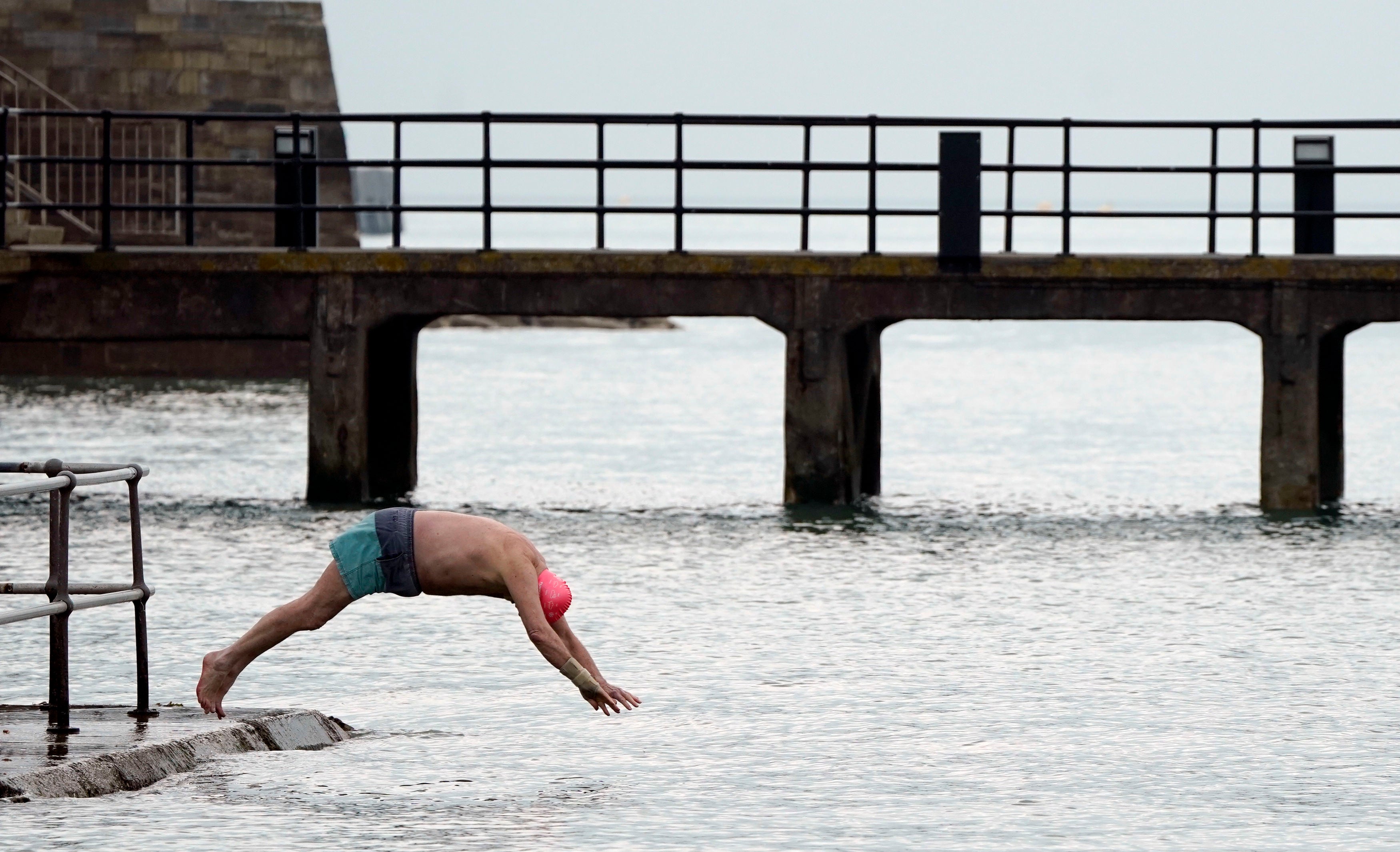 A person dives into the sea next to the Hot Walls in Old Portsmouth, an area blanketed in snow this morning