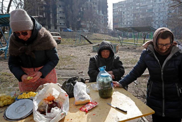 <p>Local residents cook food outside a damaged apartment building in Mariupol</p>