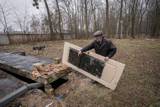 <p>Un hombre levanta una puerta que cubre la abertura de un recinto subterráneo en el que se arrojan los cuerpos de civiles asesinados por las fuerzas rusas</p>