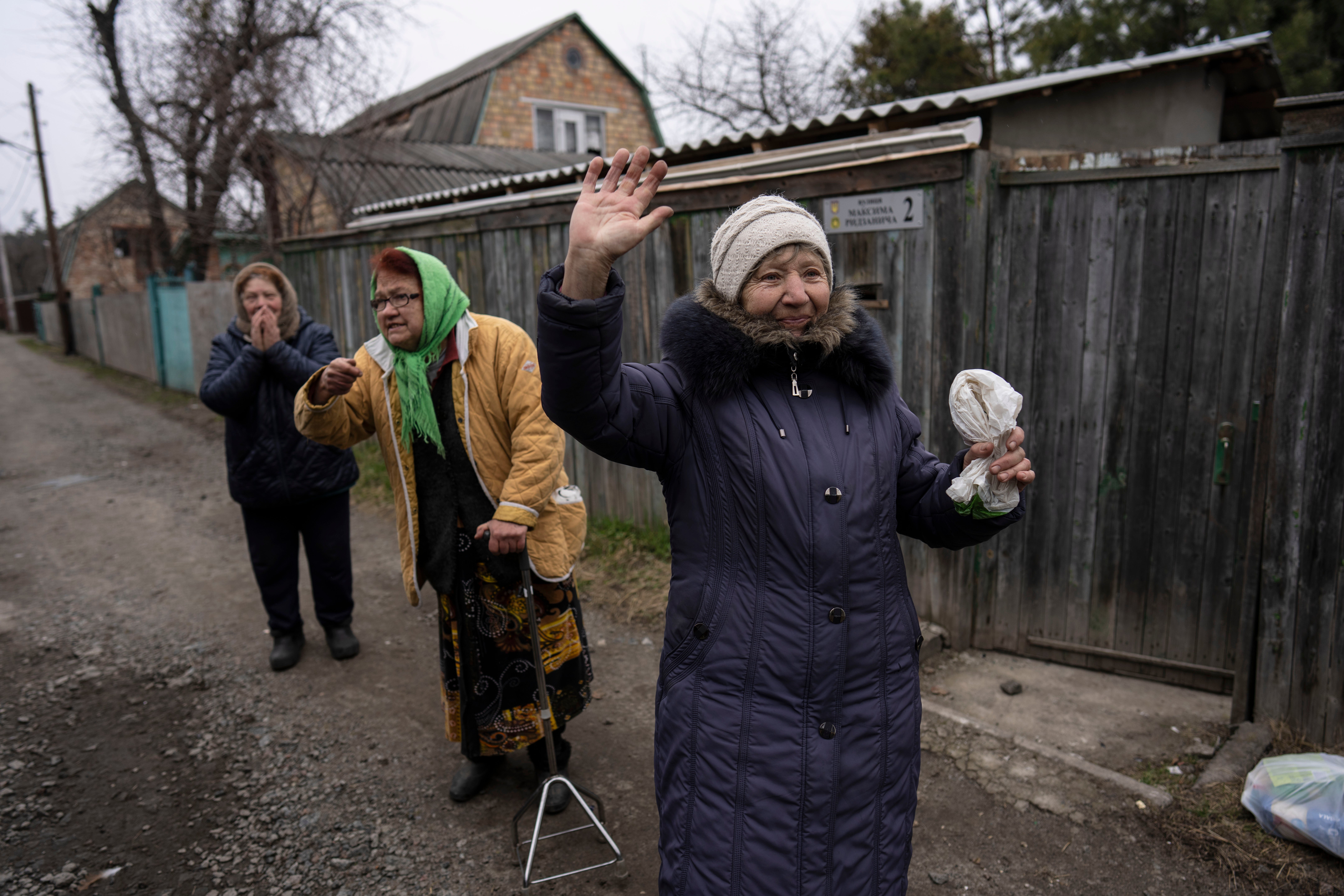 Neighbours of three men killed in the courtyard of a house wave to reporters covering the scene in Bucha, on the outskirts of Kyiv (Rodrigo Abd/AP)