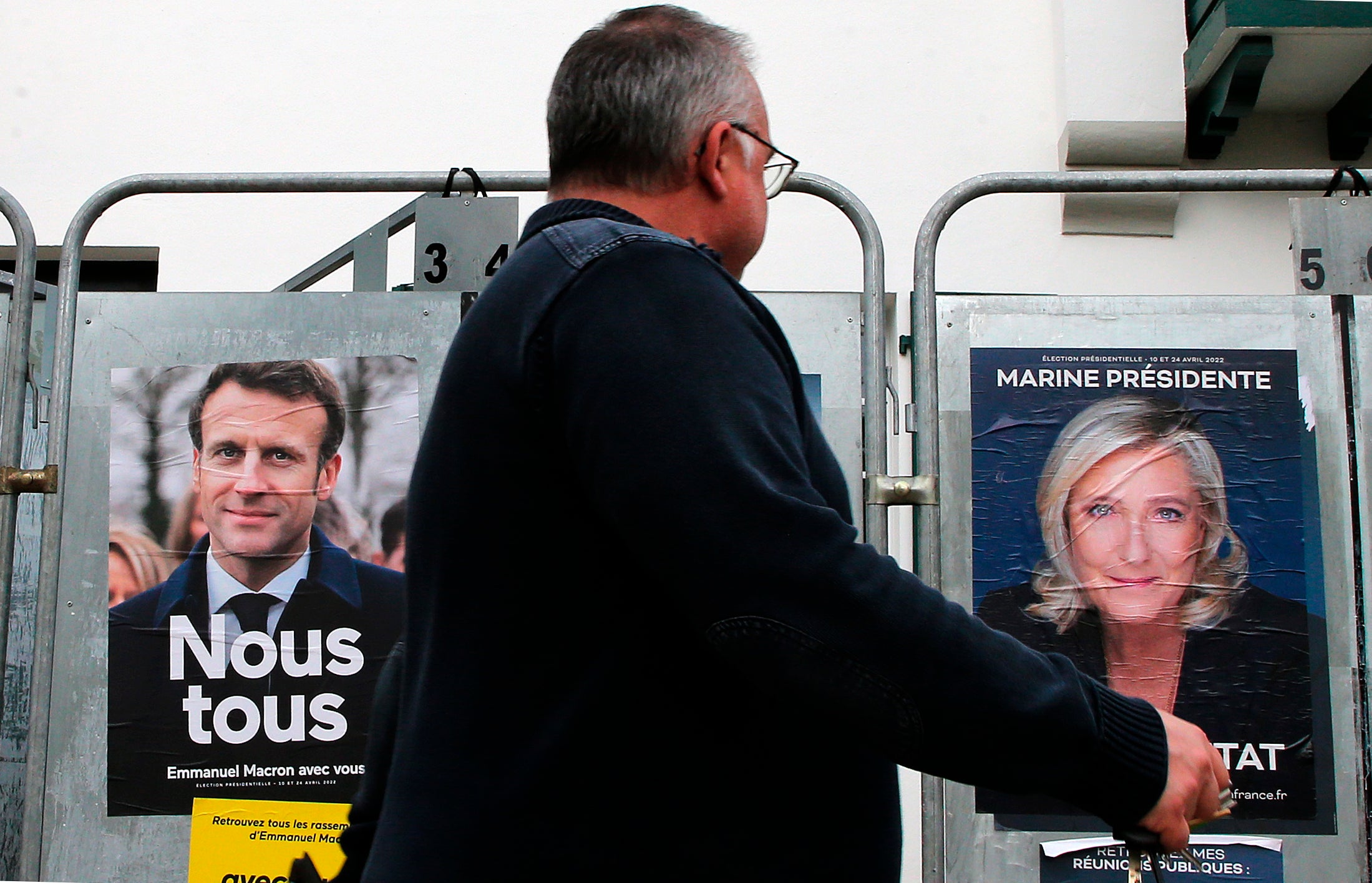 A man walks past presidential campaign posters of Macron and Le Pen in Anglet, southwestern France, 8 April 2022