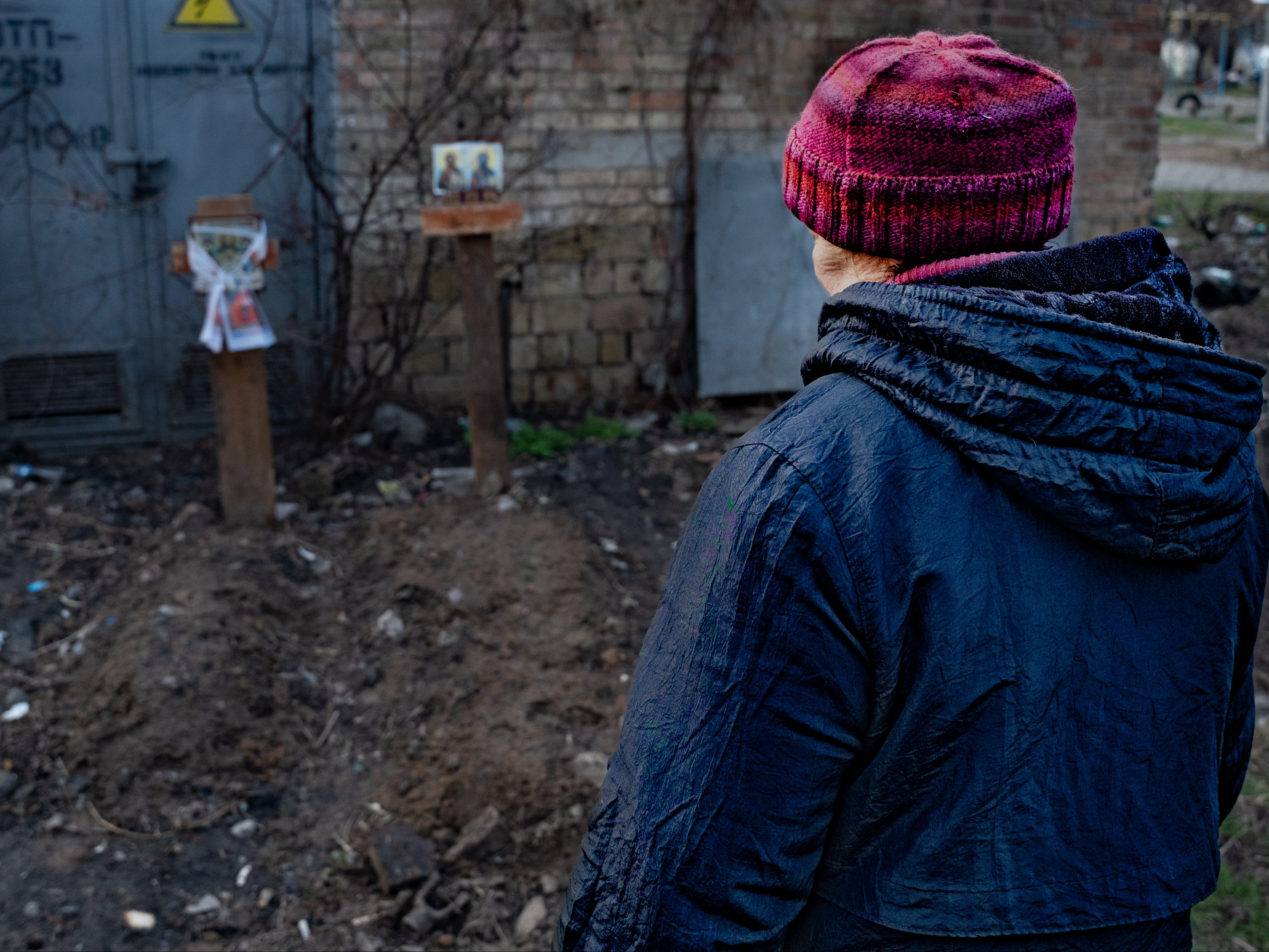 Helena prays by the graves she helped dig outside her flat window in Bucha