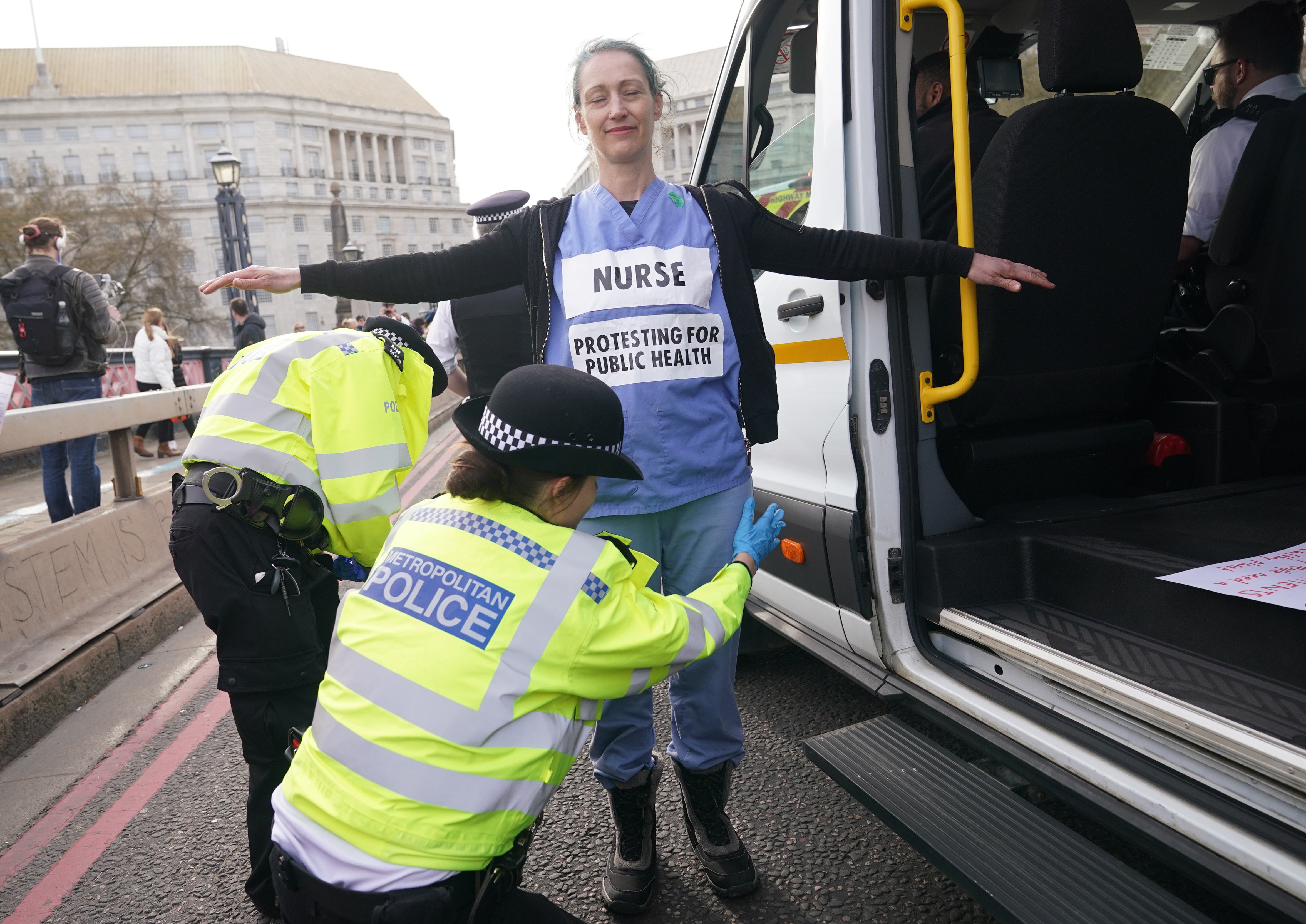 A protestor in nurse’s scrubs is searched by police on Lambeth Bridge (Yui Mok/PA)