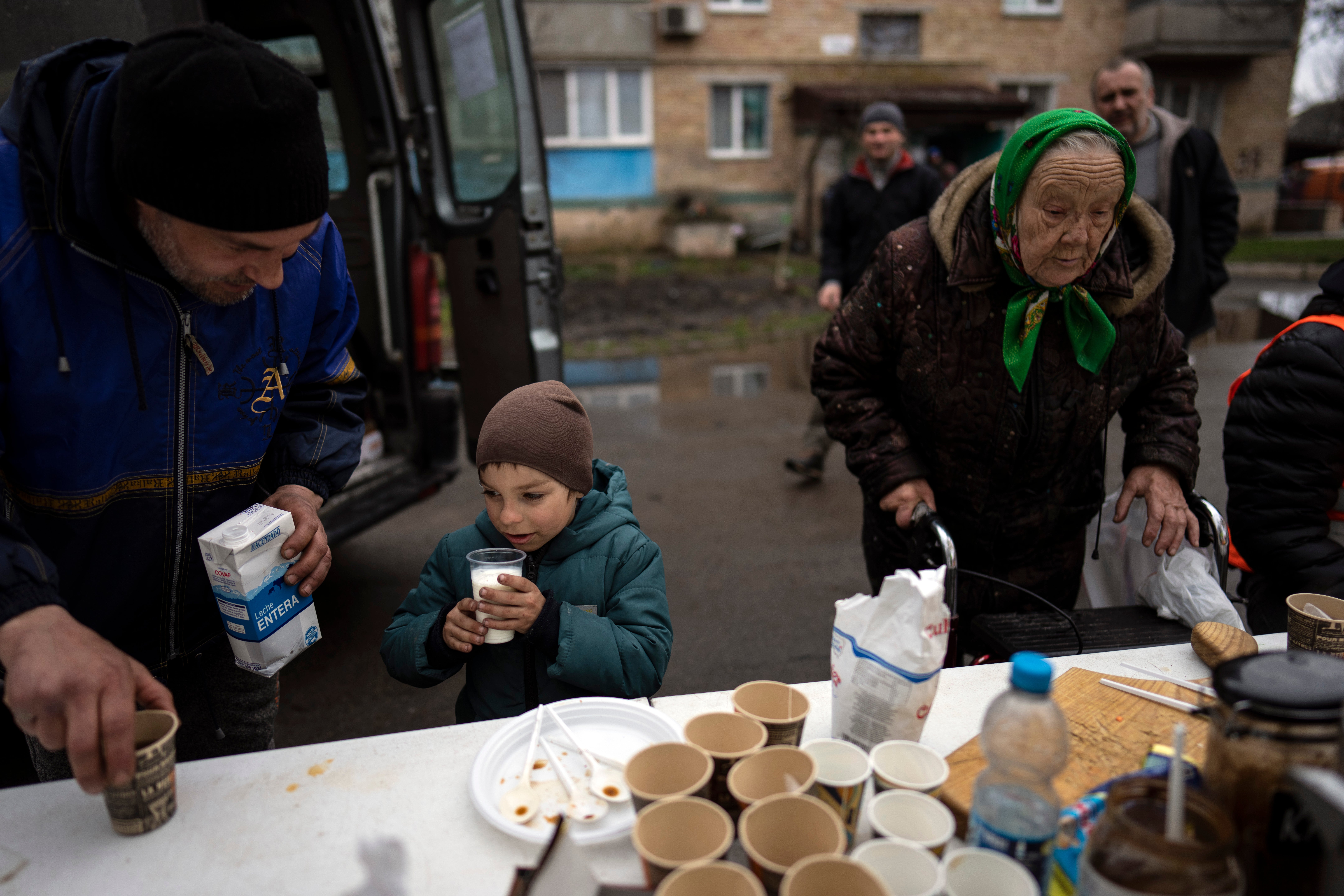 Vlad, 6, drinks milk next to his father Ivan, 40, at a donated food distribution stand in Bucha, in the outskirts of Kyiv, Ukraine