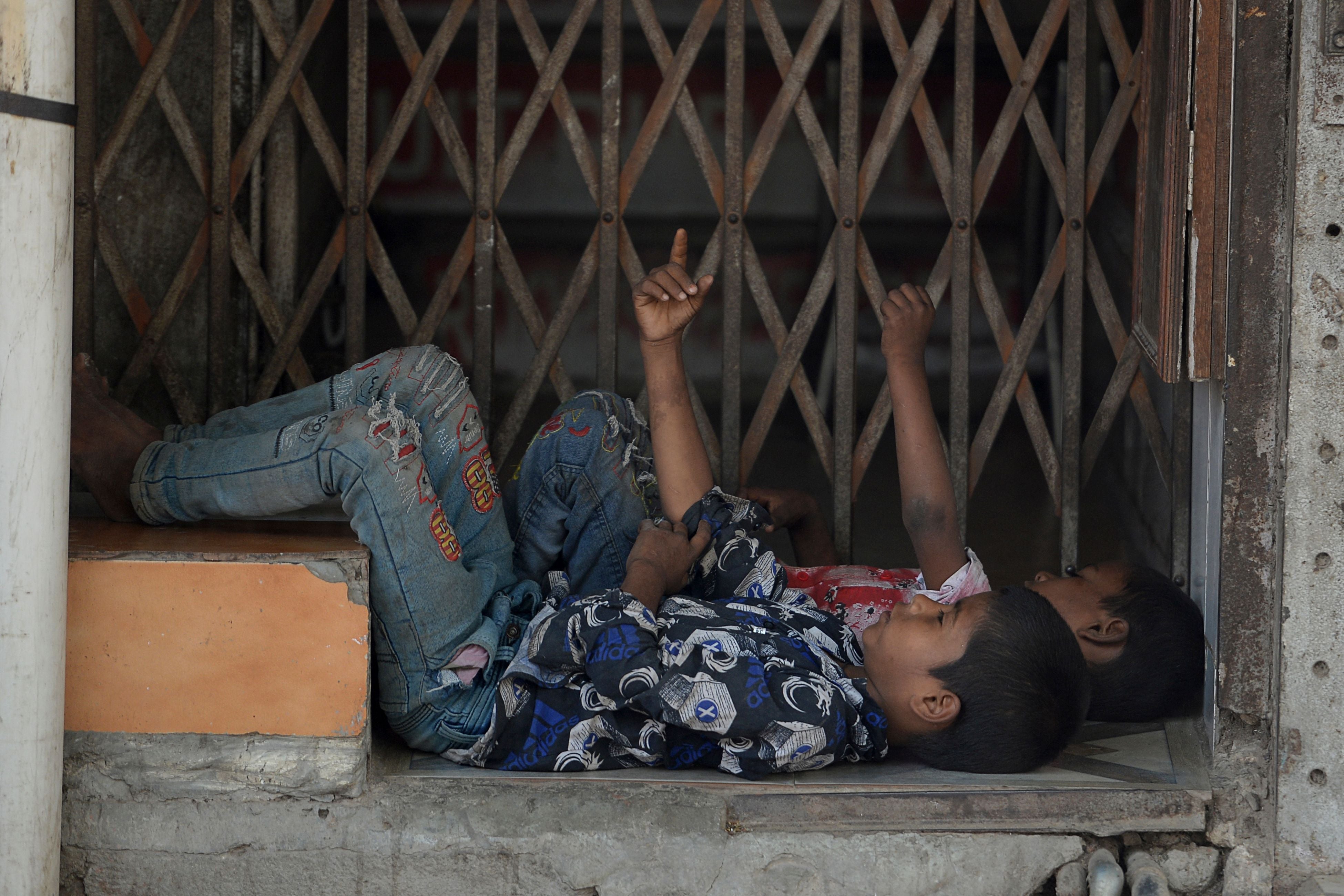 File: Children from a low income neighbourhood rest in front of a closed shop during a lockdown in Delhi