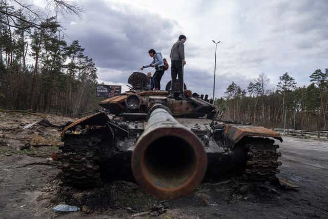 Local residents stand atop of a Russian tank damaged during fighting between Russian and Ukrainian forces in the outskirts of Kyiv, Ukraine (Evgeniy Maloletka/AP)