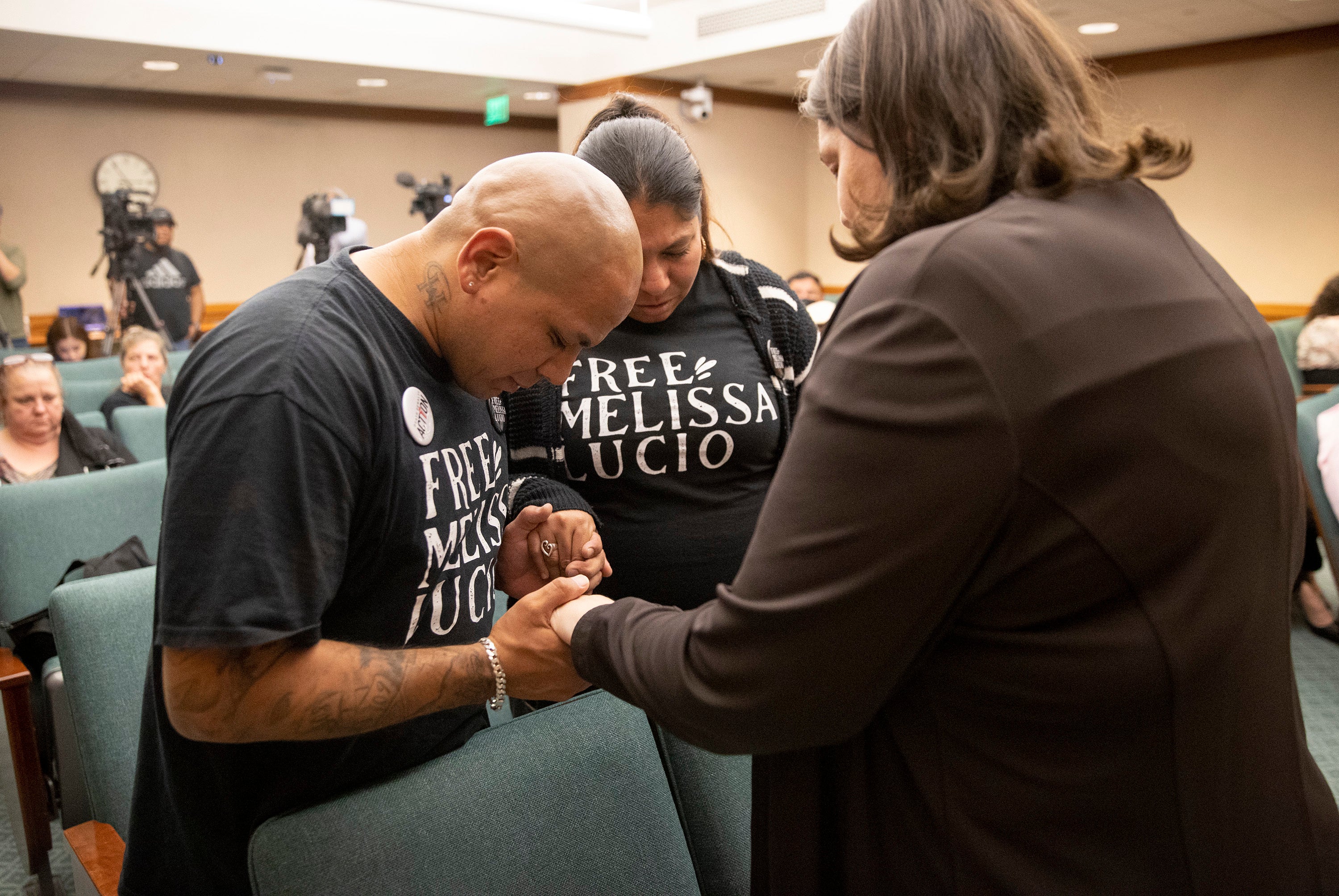 Melissa’s son John Lucio, with his wife, Michelle Lucio, prays with Jennifer Allmon, right, Executive Director of the Texas Catholic Church at a hearing last week