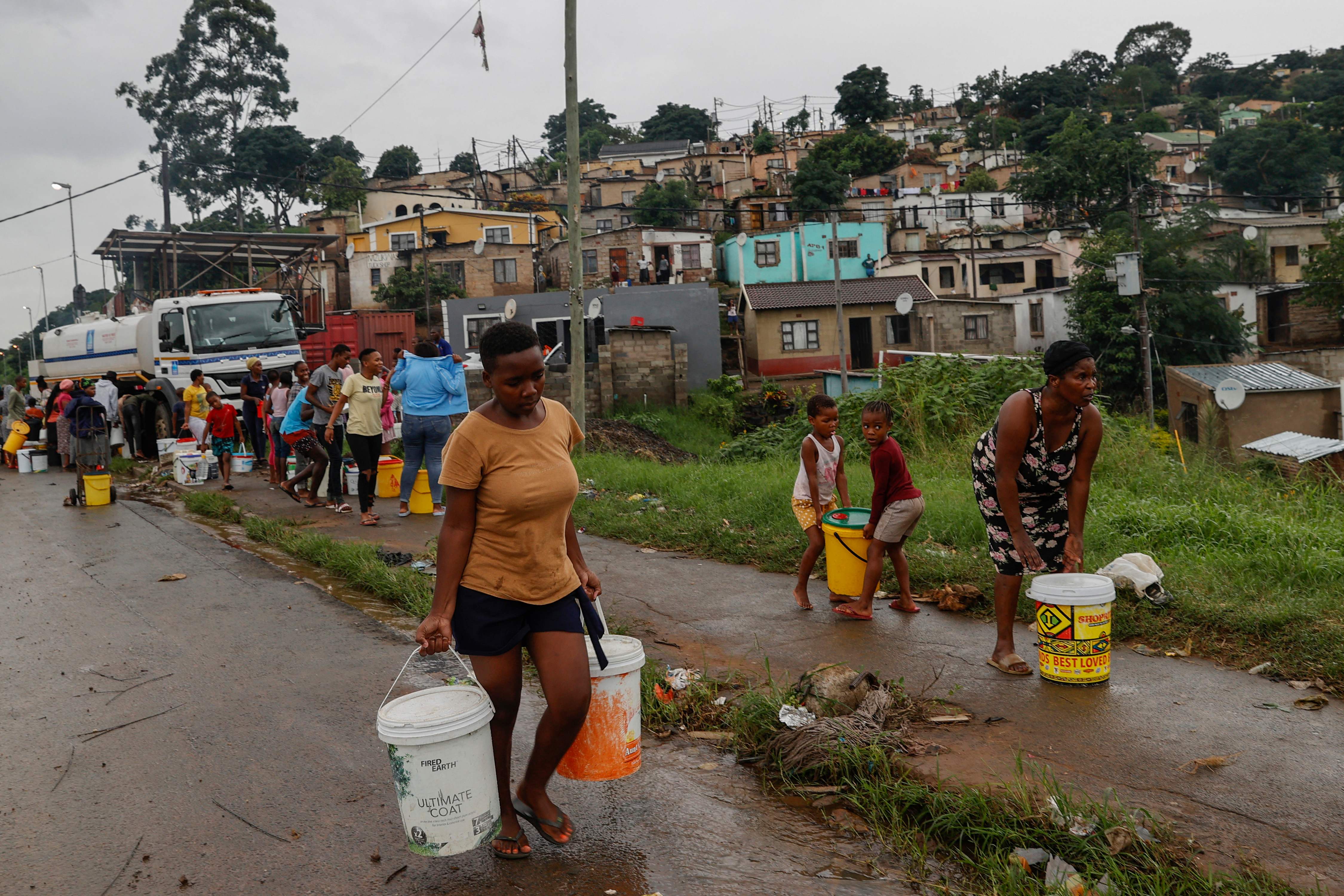 Residents of Bhambayi settlement walk with buckets filled with water after the floods