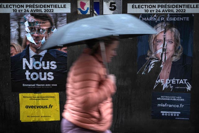 <p>A woman walks past posters for the two candidates in Paris</p>