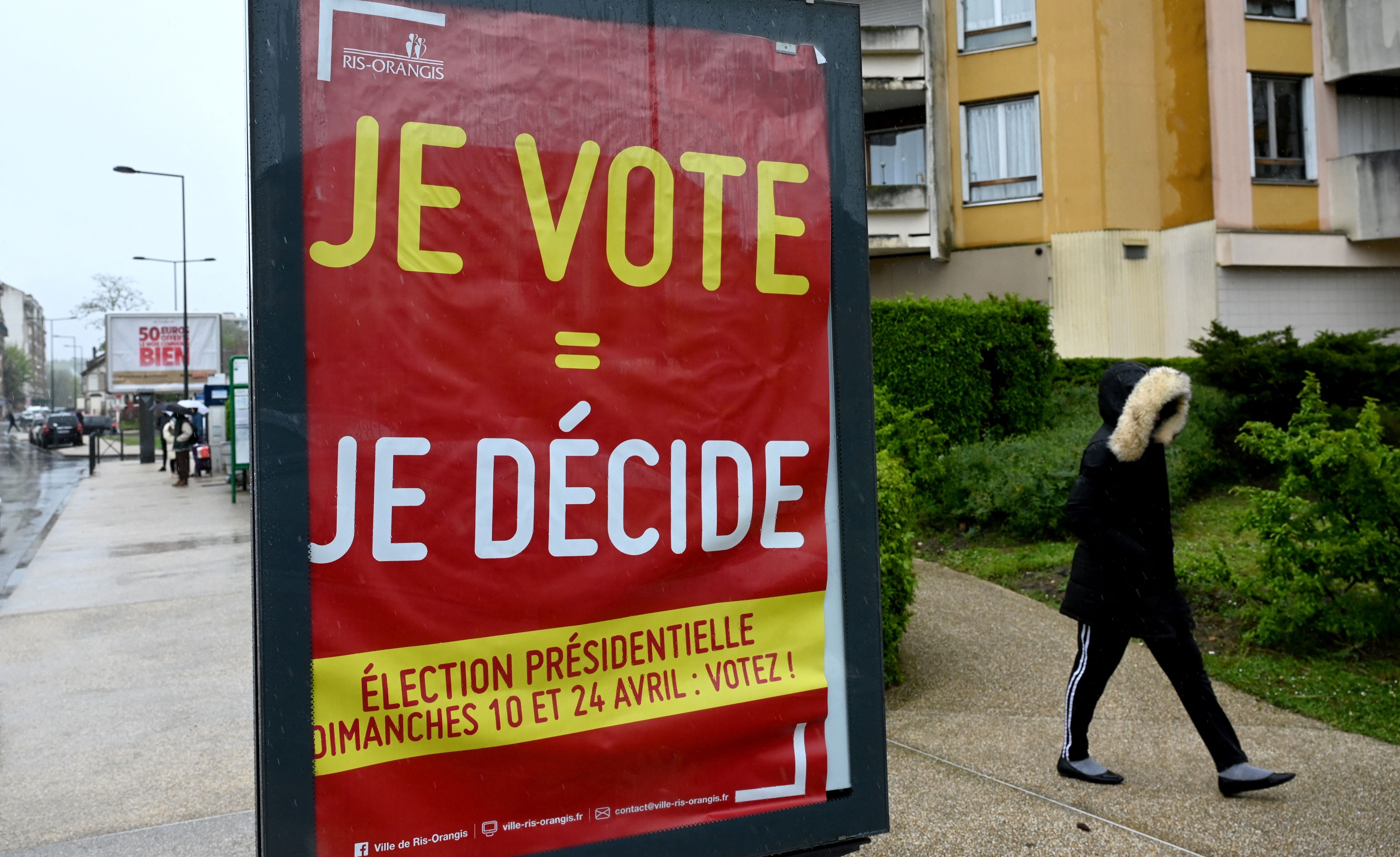 A pedestrian walks past a poster reading ‘I vote = I decide’ in the Paris suburb of Ris-Orangis
