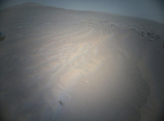 <p>The shadow of Ingenuity, Nasa’s Mars helicopter, can be seen to the lower left as the vehicle soars above the Martian landscape</p>