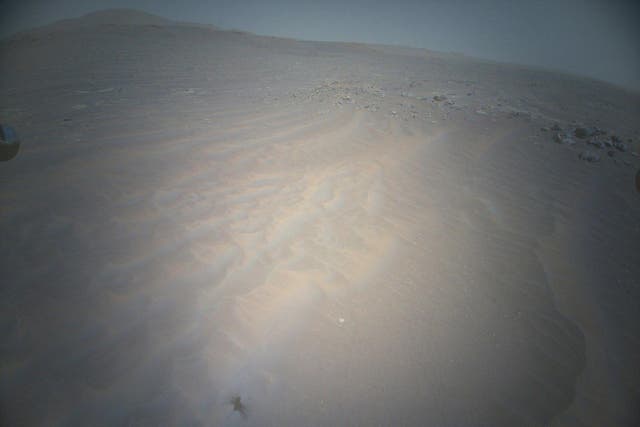 <p>The shadow of Ingenuity, Nasa’s Mars helicopter, can be seen to the lower left as the vehicle soars above the Martian landscape</p>