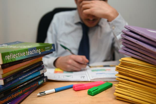 A teacher marking books (PA)