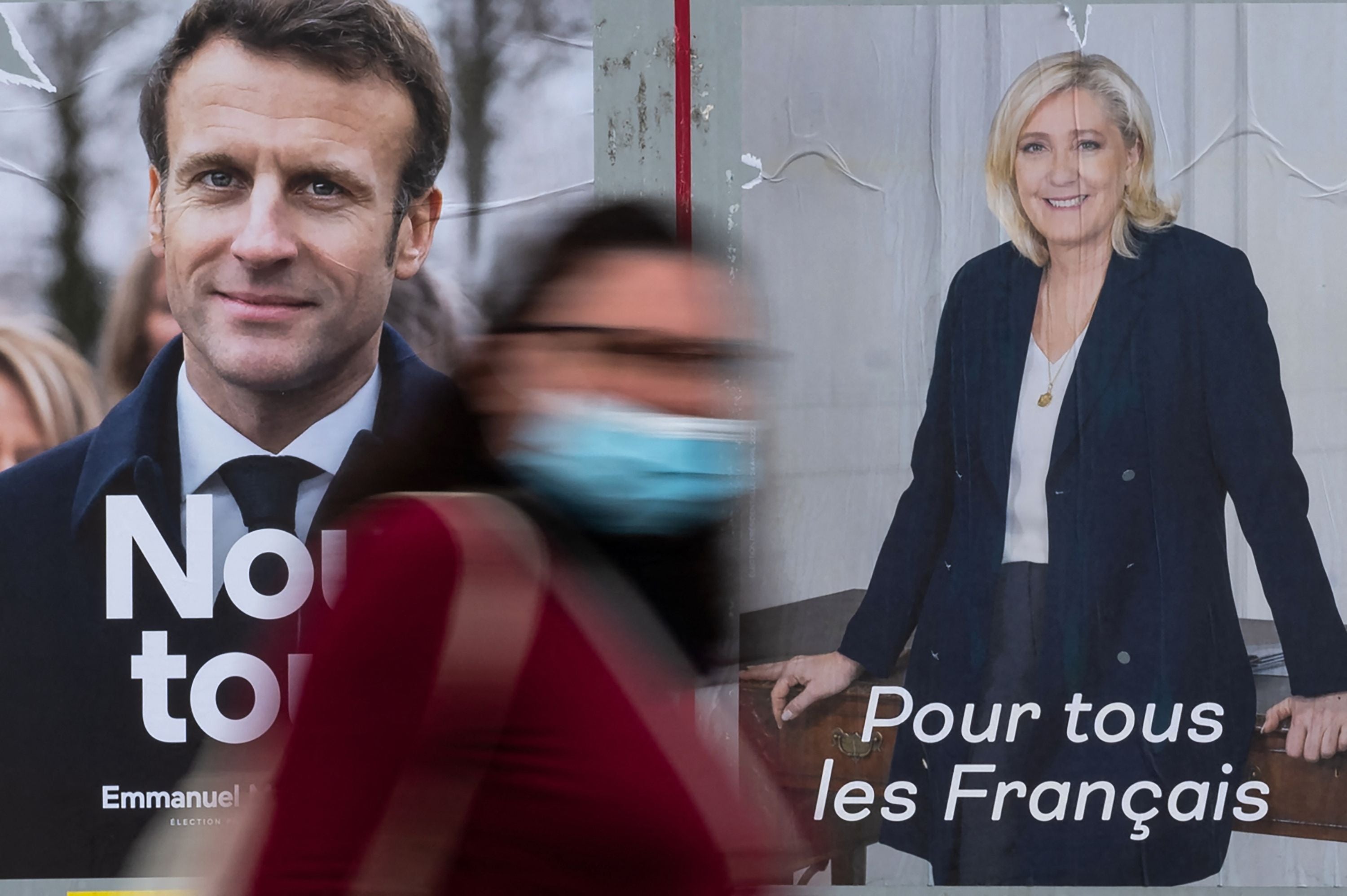 A woman passes by electoral campaign posters of Emmanuel Macron and Marine Le Pen