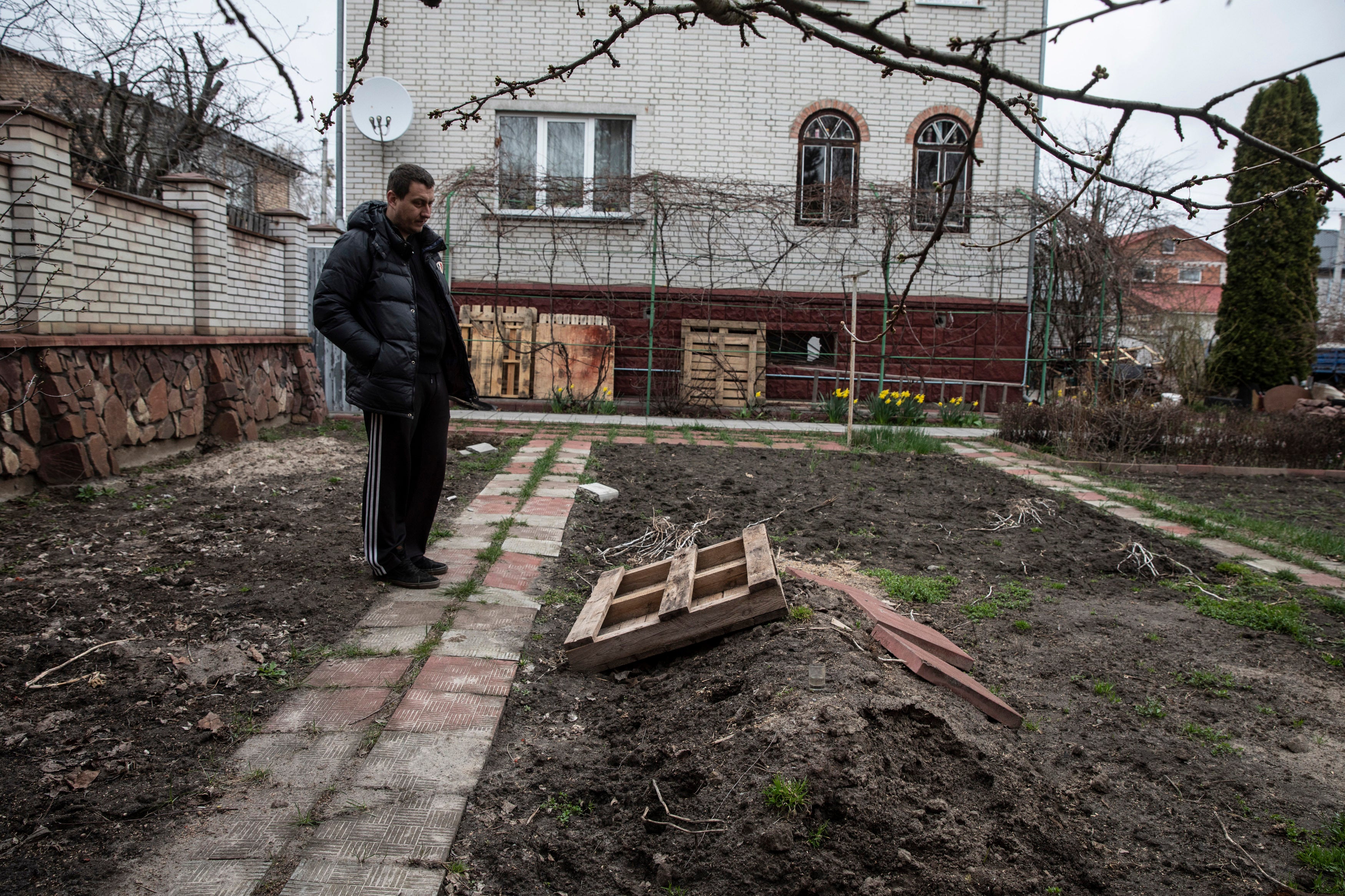 Pavlo Prykhodko stands by his father's grave in the backyard of his parent's home in Vorzel, Ukraine