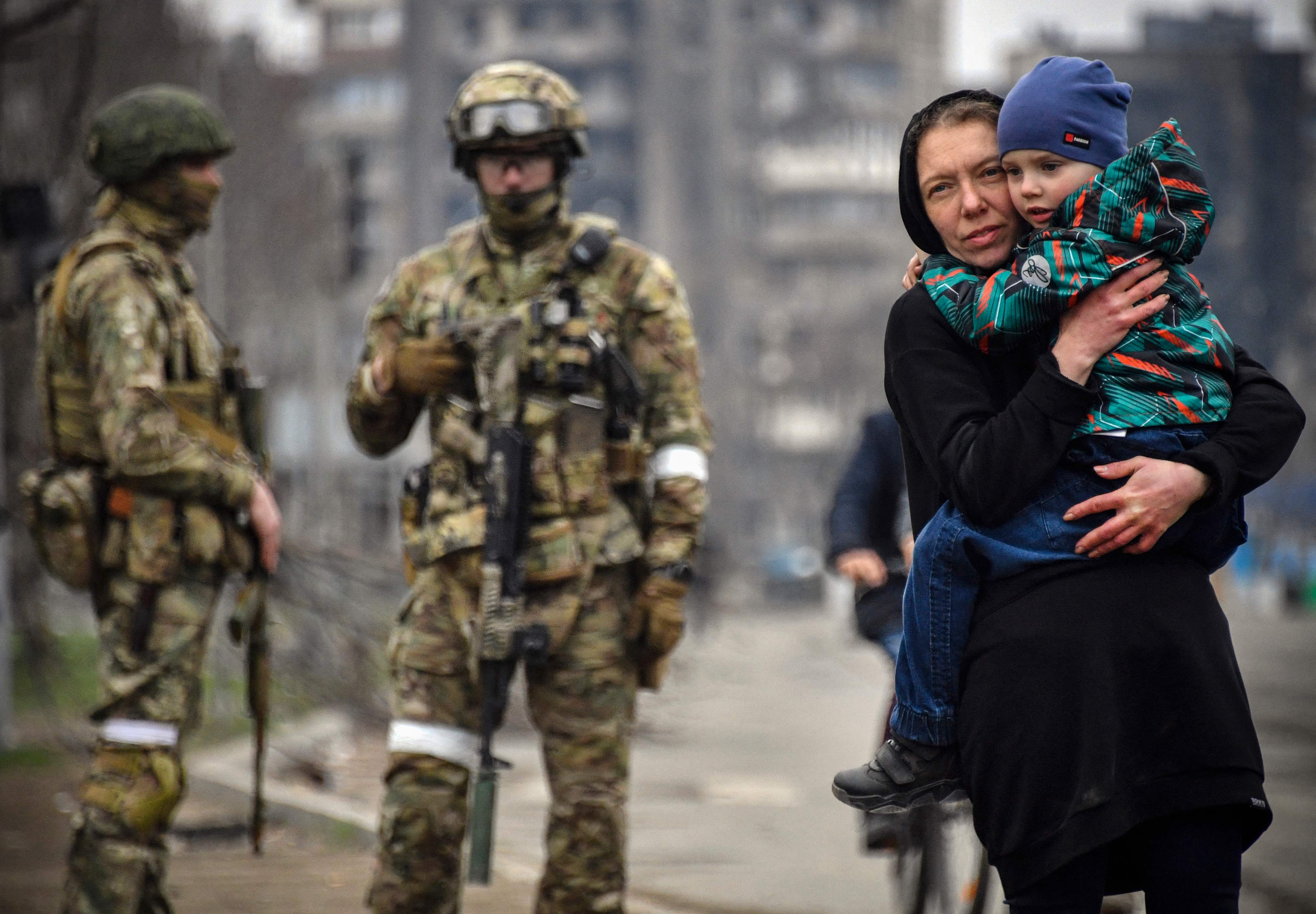 A woman holds a child next to Russian soldiers in a street of Mariupol