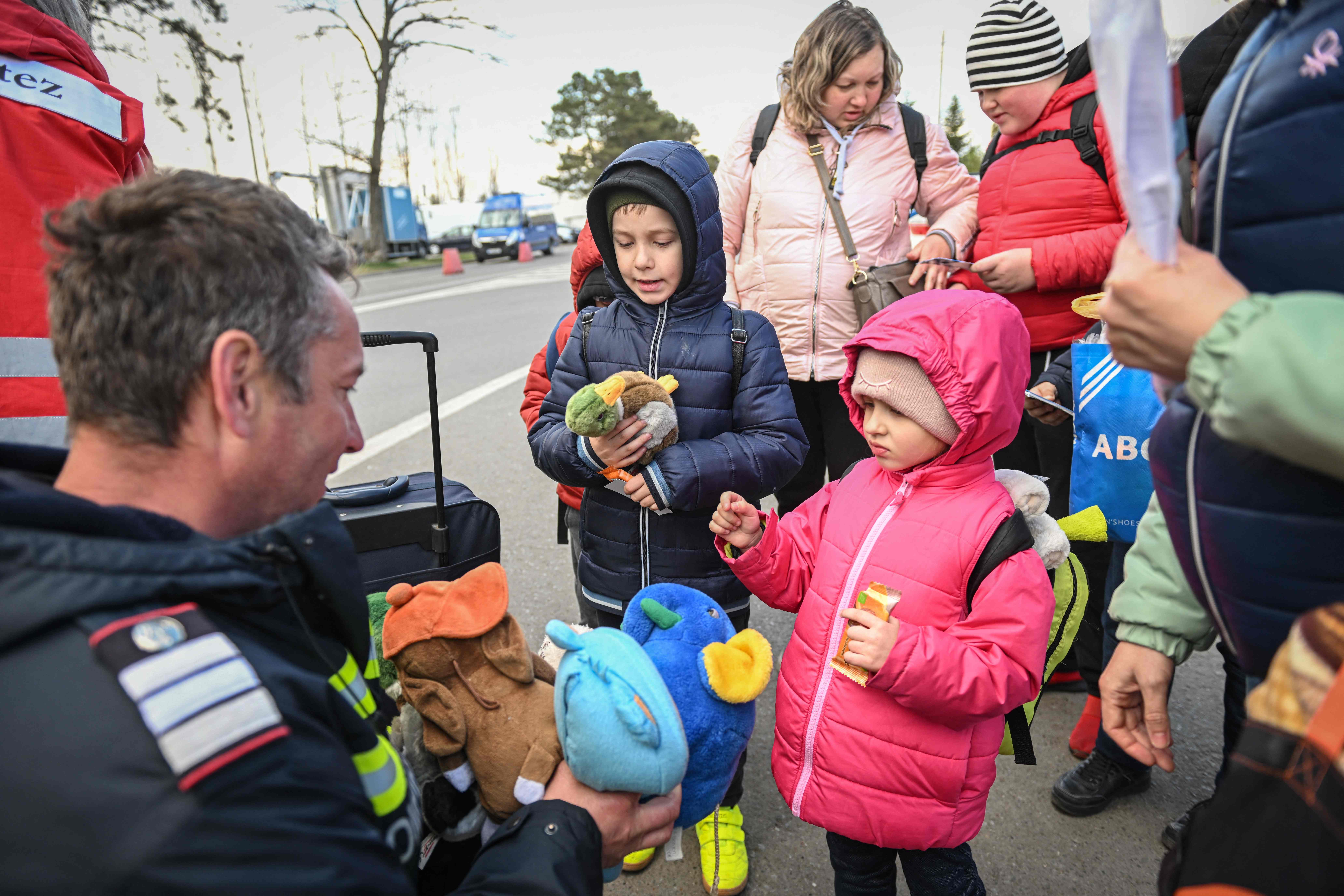 Ukrainian refugee children receive soft toys from a Romanian fireman after arriving at the Siret border crossing between Romania and Ukraine