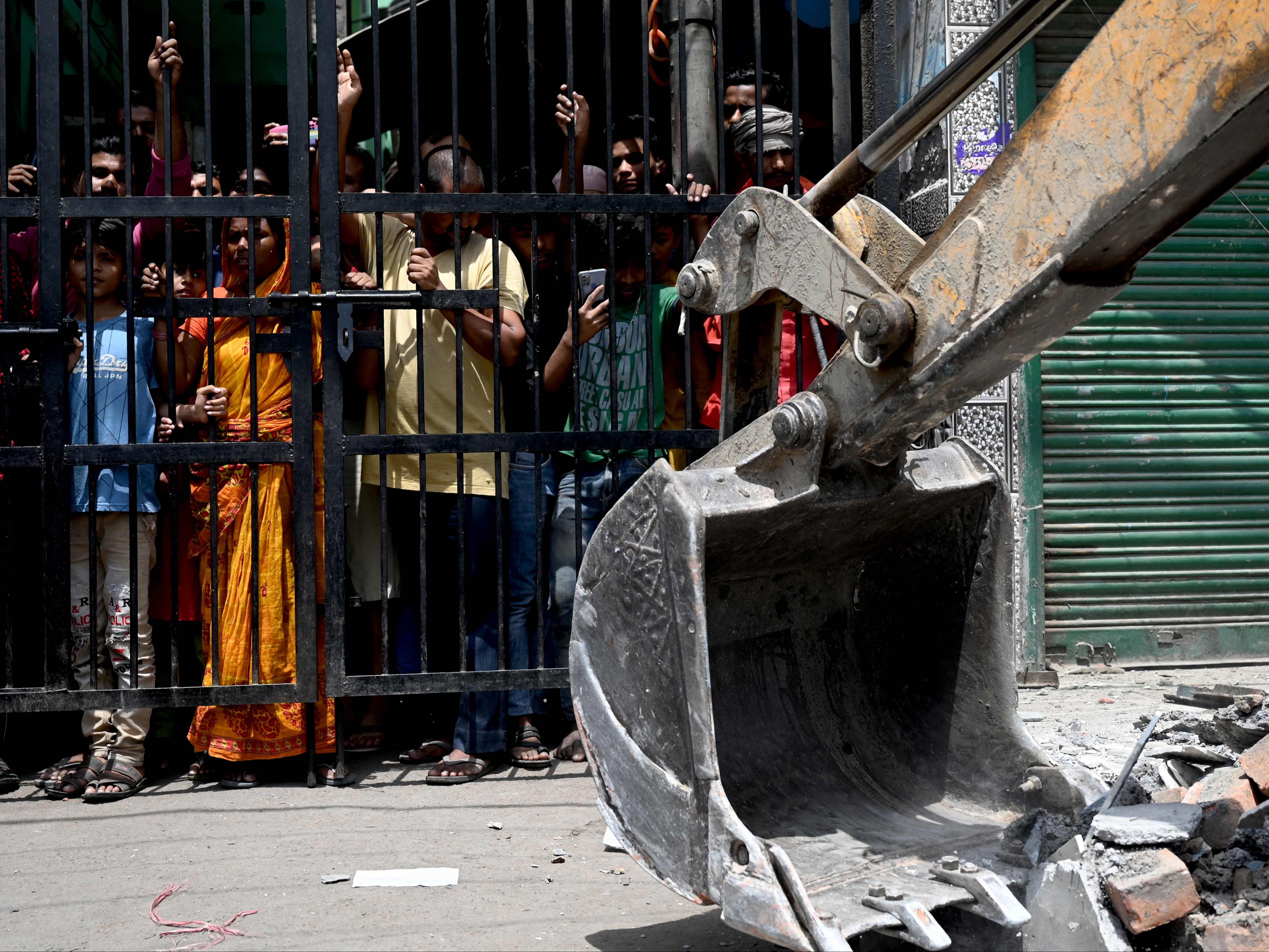 Residents watch as a bulldozer demolishes an illegal structure in a residential area of Jahangirpuri in New Delhi on 21 April