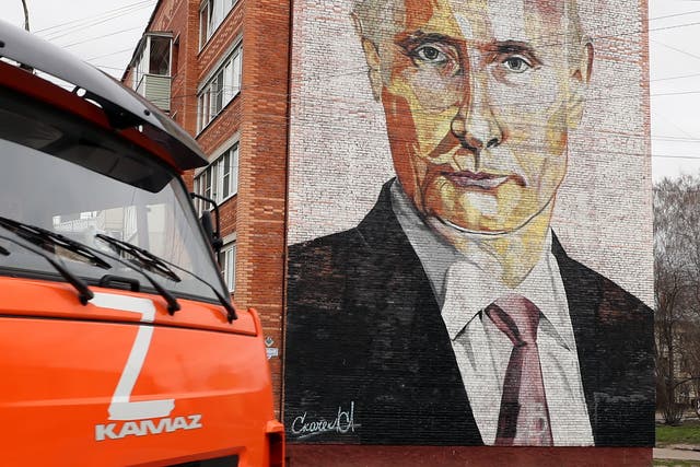 <p>A truck with the letter Z drives down a street in front of a block of flats with a mural depicting Russian President Vladimir Putin </p>
