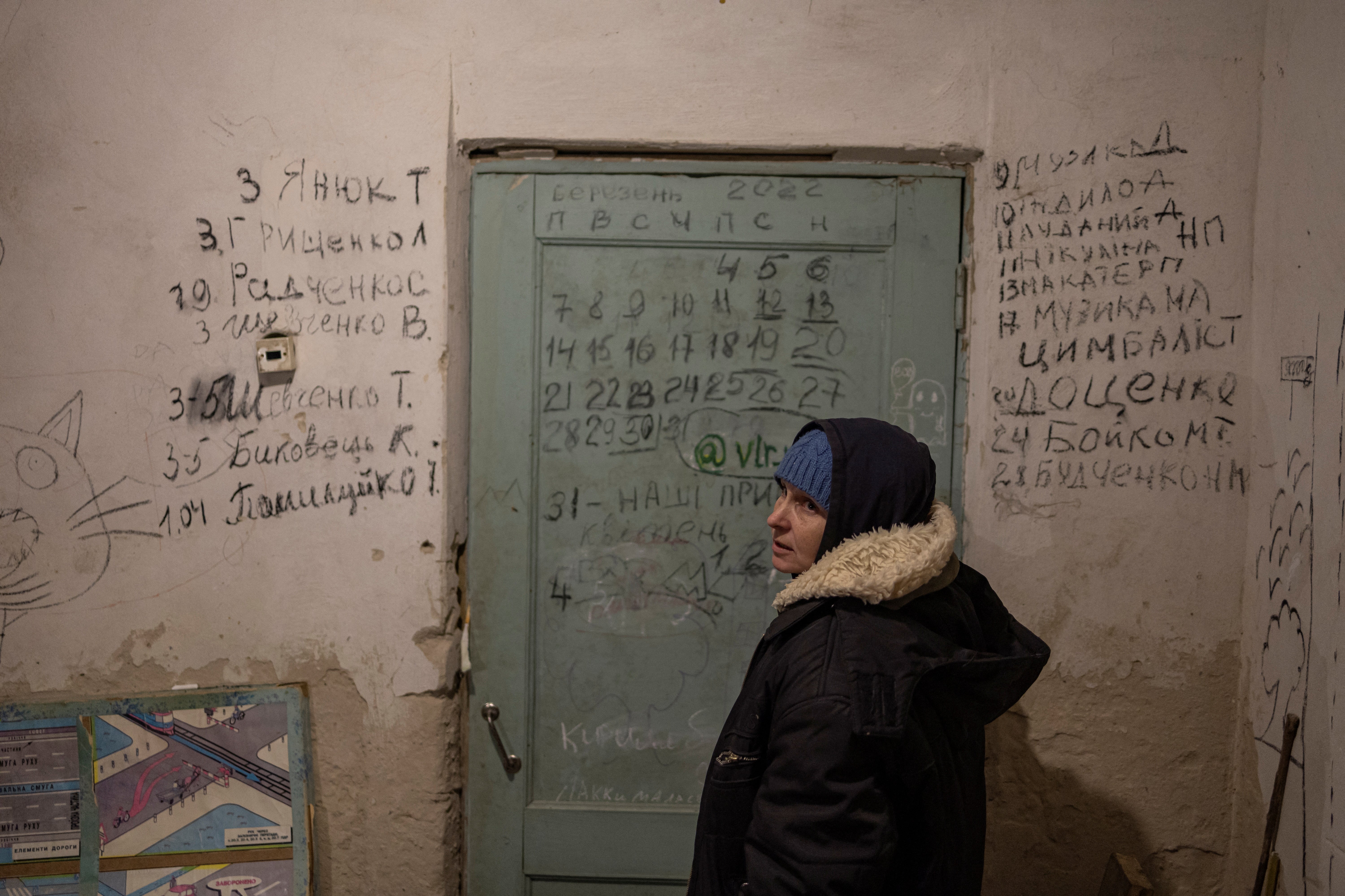 Halyna Tolochina stands in front of a wall inscribed with the names of the dead in the village of Yahidne, Ukraine