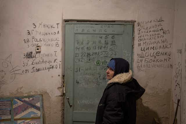 <p>Halyna Tolochina stands in front of a wall inscribed with the names of the dead in the village of Yahidne, Ukraine</p>