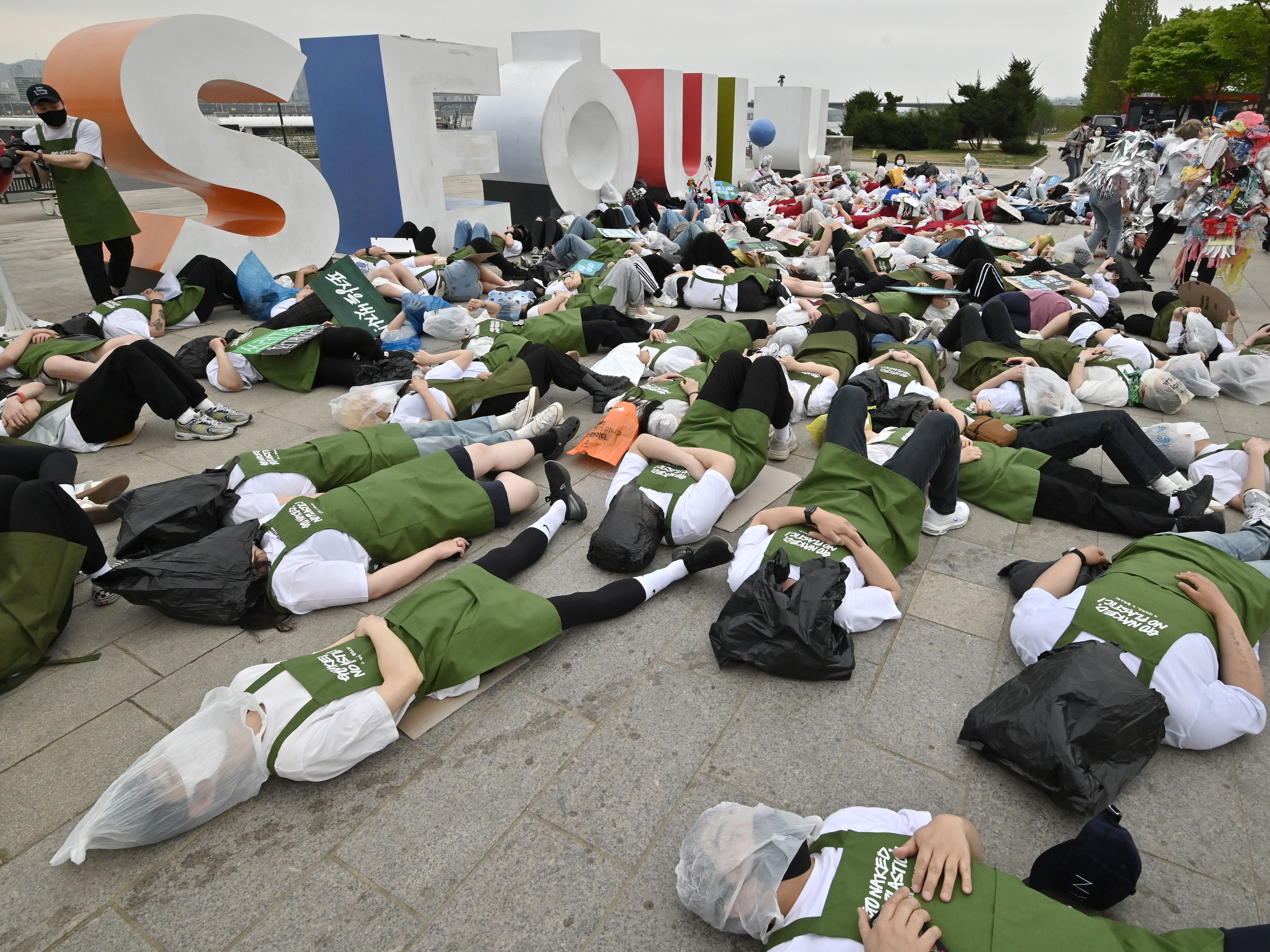 South Korean environmental activists lie on the ground with plastic waste during a campaign marking Earth Day at a park along the Han River in Seoul