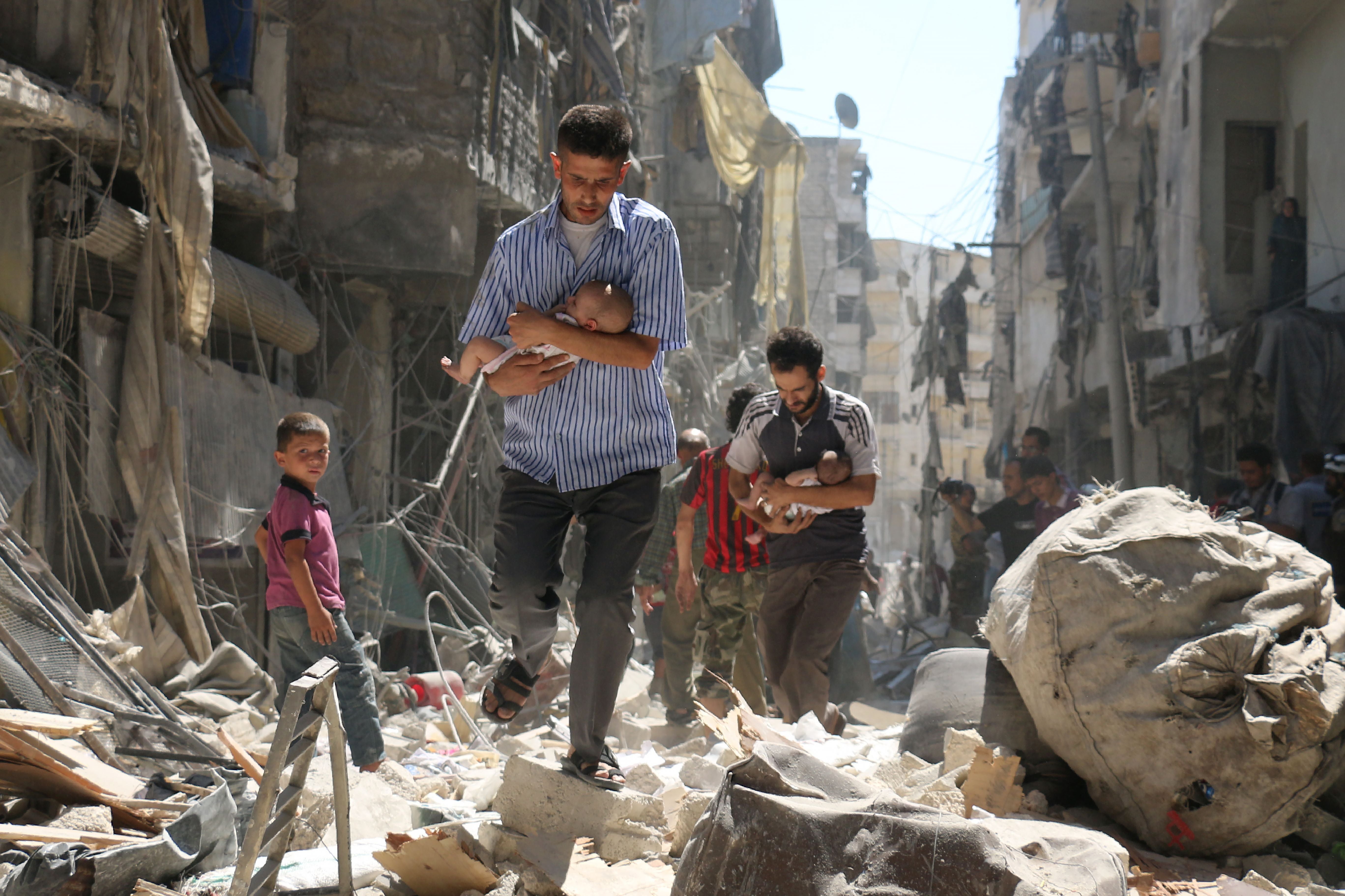 Syrian men carrying babies make their way through the rubble of destroyed buildings following an air strike on the rebel-held Salihin neighbourhood of Aleppo