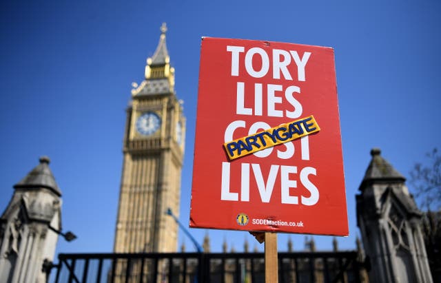 <p>A protester holds up a placard outside Parliament in London as Johnson faces continued pressure over allegations he broke lockdown regulations</p>