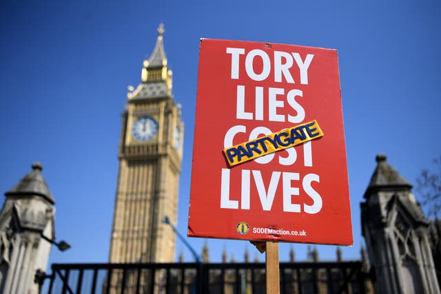 <p>A protester holds up a placard outside Parliament in London as Johnson faces continued pressure over allegations he broke lockdown regulations</p>
