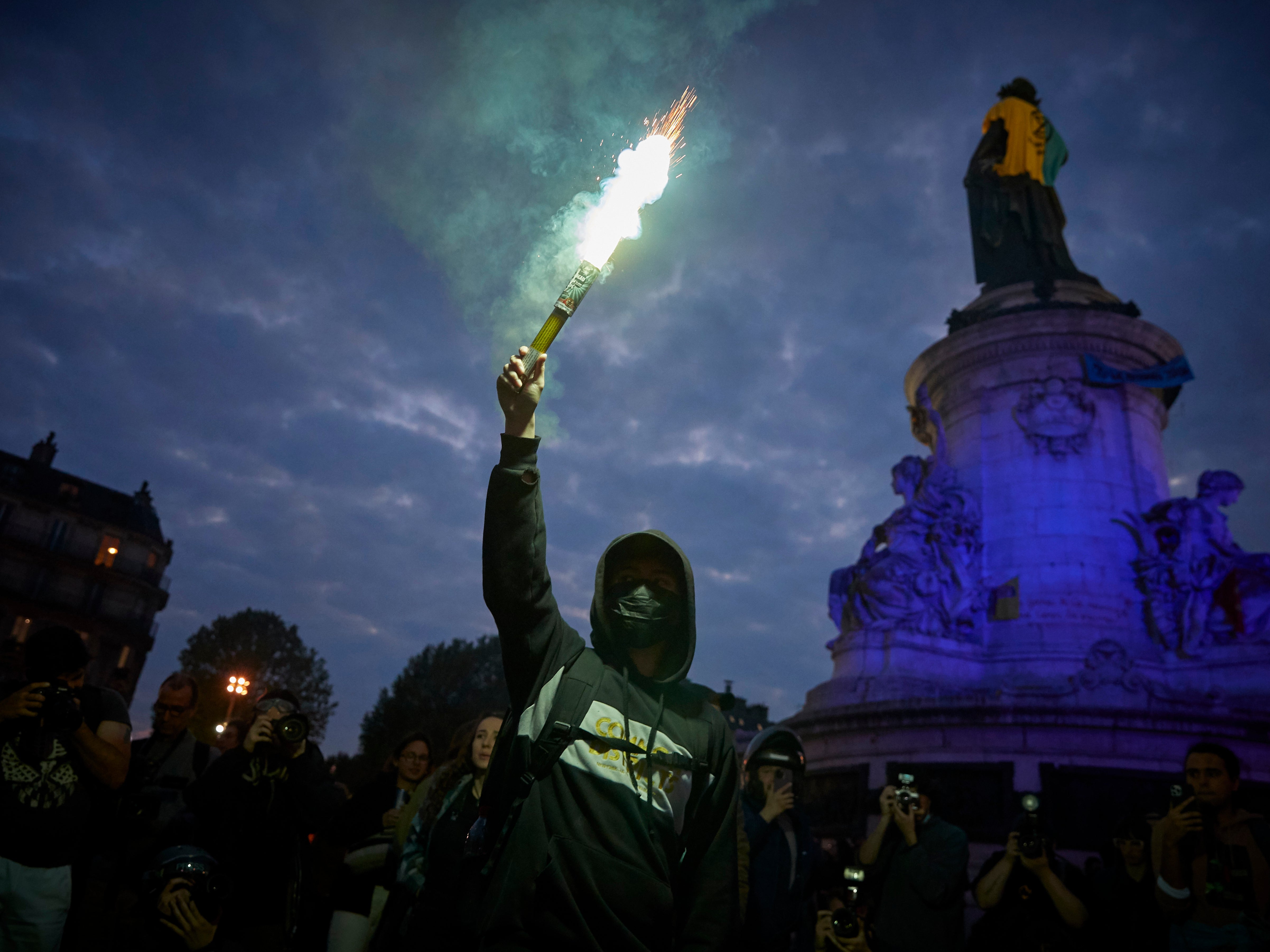 A teenage boy holds up a flare as people protest the election result in central Paris