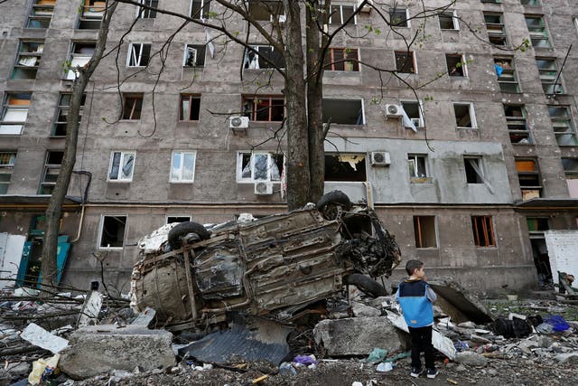 <p>A boy stands next to a wrecked vehicle in front of an apartment building in the southern port city of Mariupol</p>