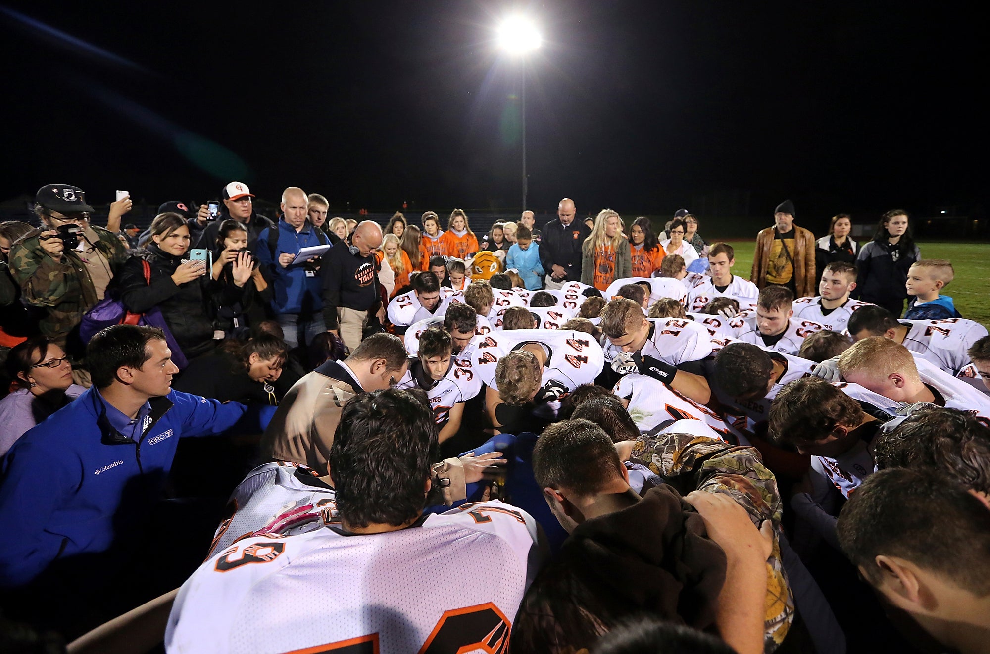 Assistant football coach Joe Kennedy is surrounded by football players as they kneel and pray with him on the field after their game in 2015.