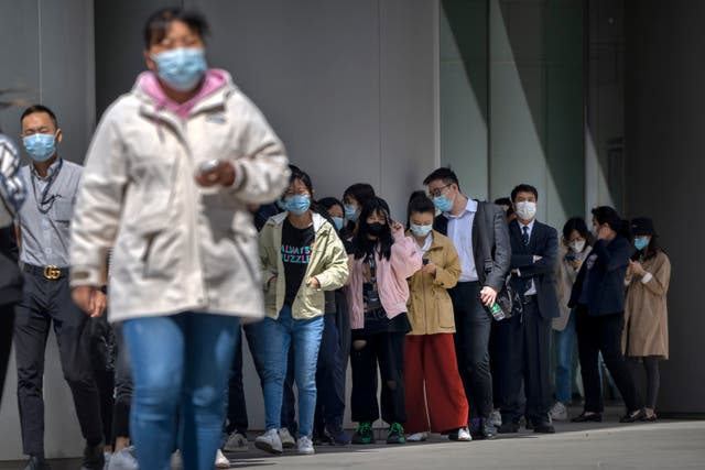 <p>People wearing face masks stand in line for coronavirus tests at an office building in the Dongcheng district of Beijing</p>