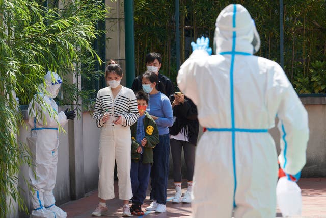<p>Community volunteers wearing personal protective equipment guide residents queuing to get tested for Covid during lockdown in Pudong district in Shanghai on April 17, 2022</p>