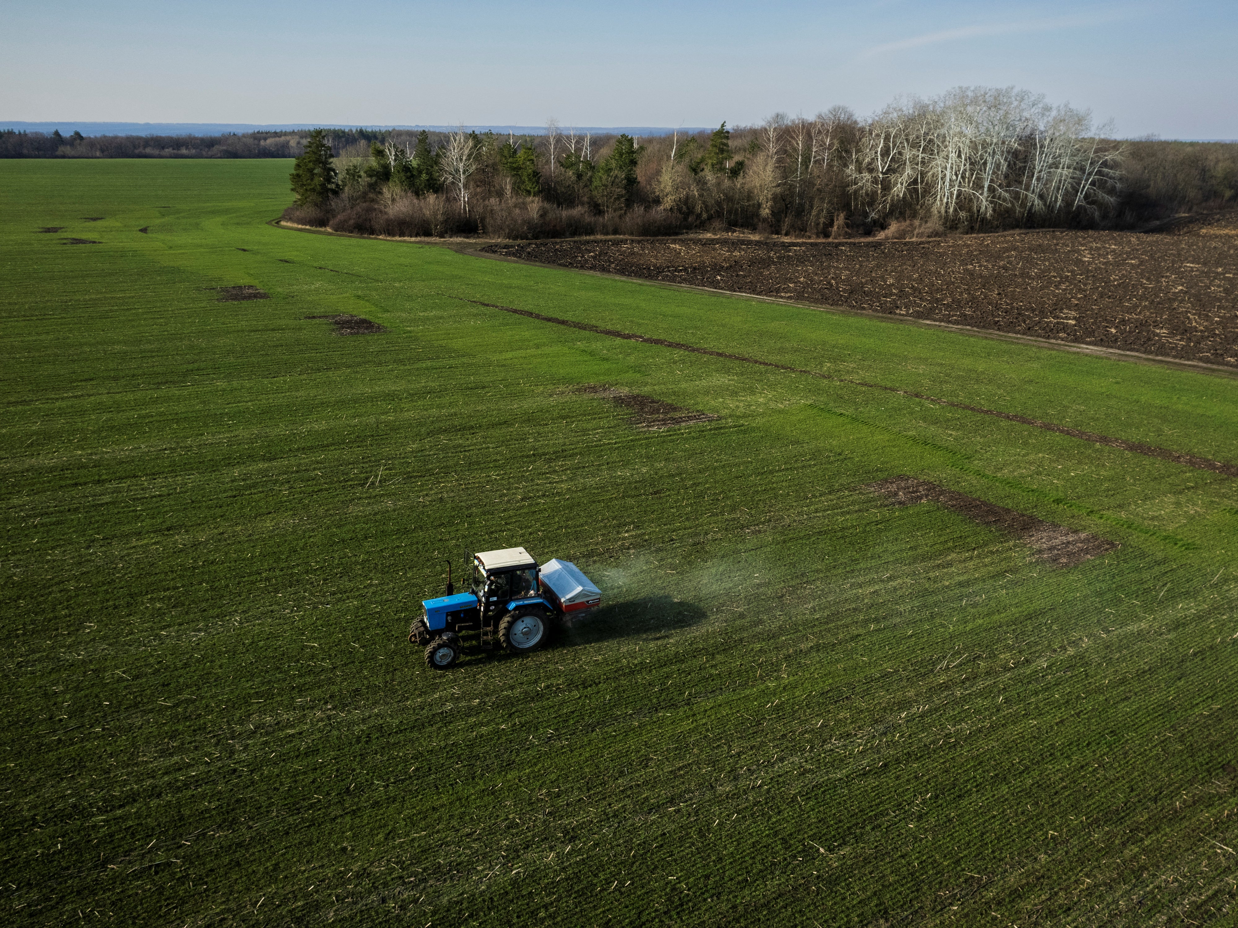<p>An aerial view shows a tractor spreading fertiliser on a wheat field near the village of Yakovlivka after it was hit by an aerial bombardment outside Kharkiv on 5 April</p>