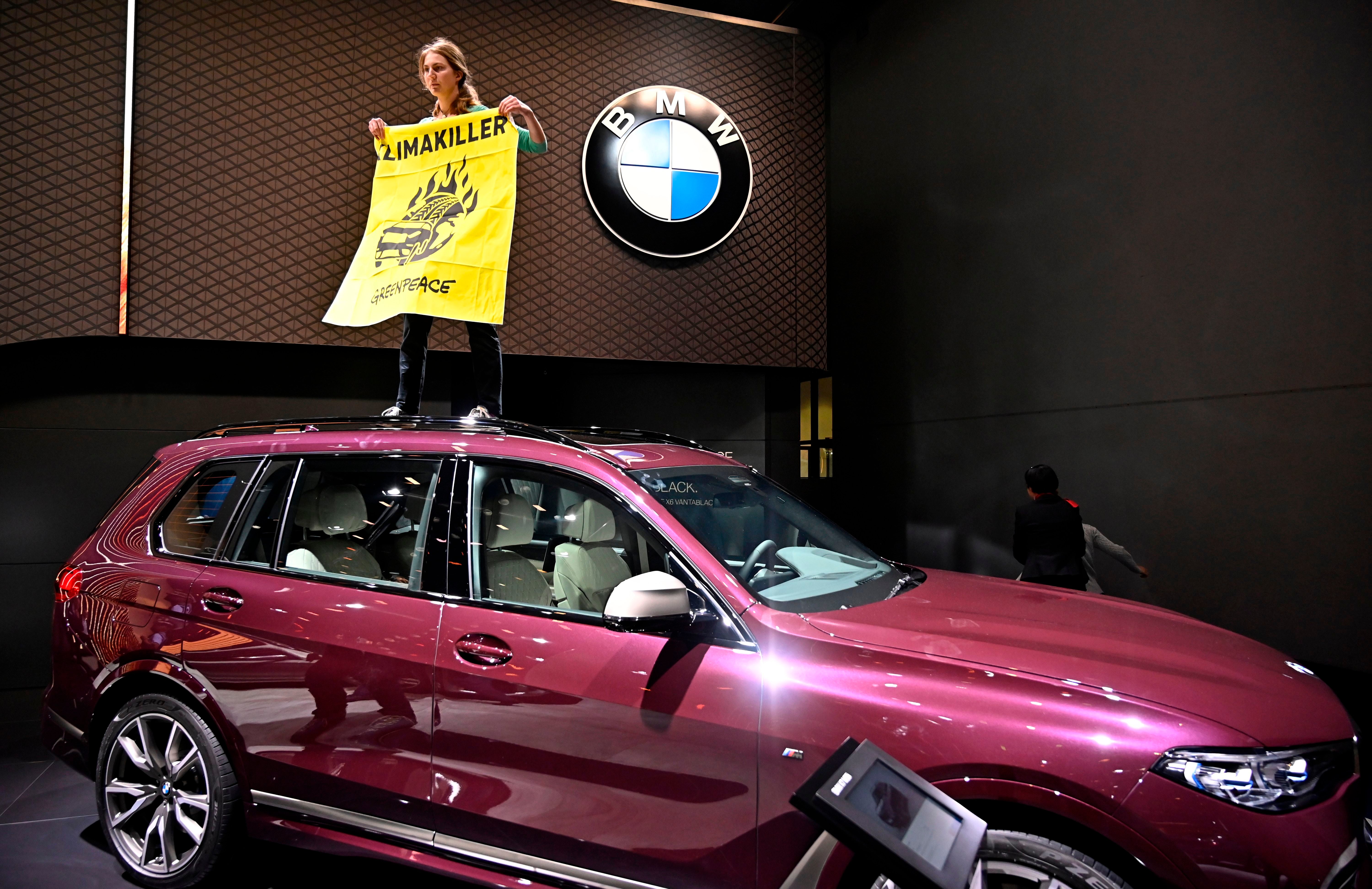 A Greenpeace activist stands on a BMW car holding a poster reading ‘climate killers’