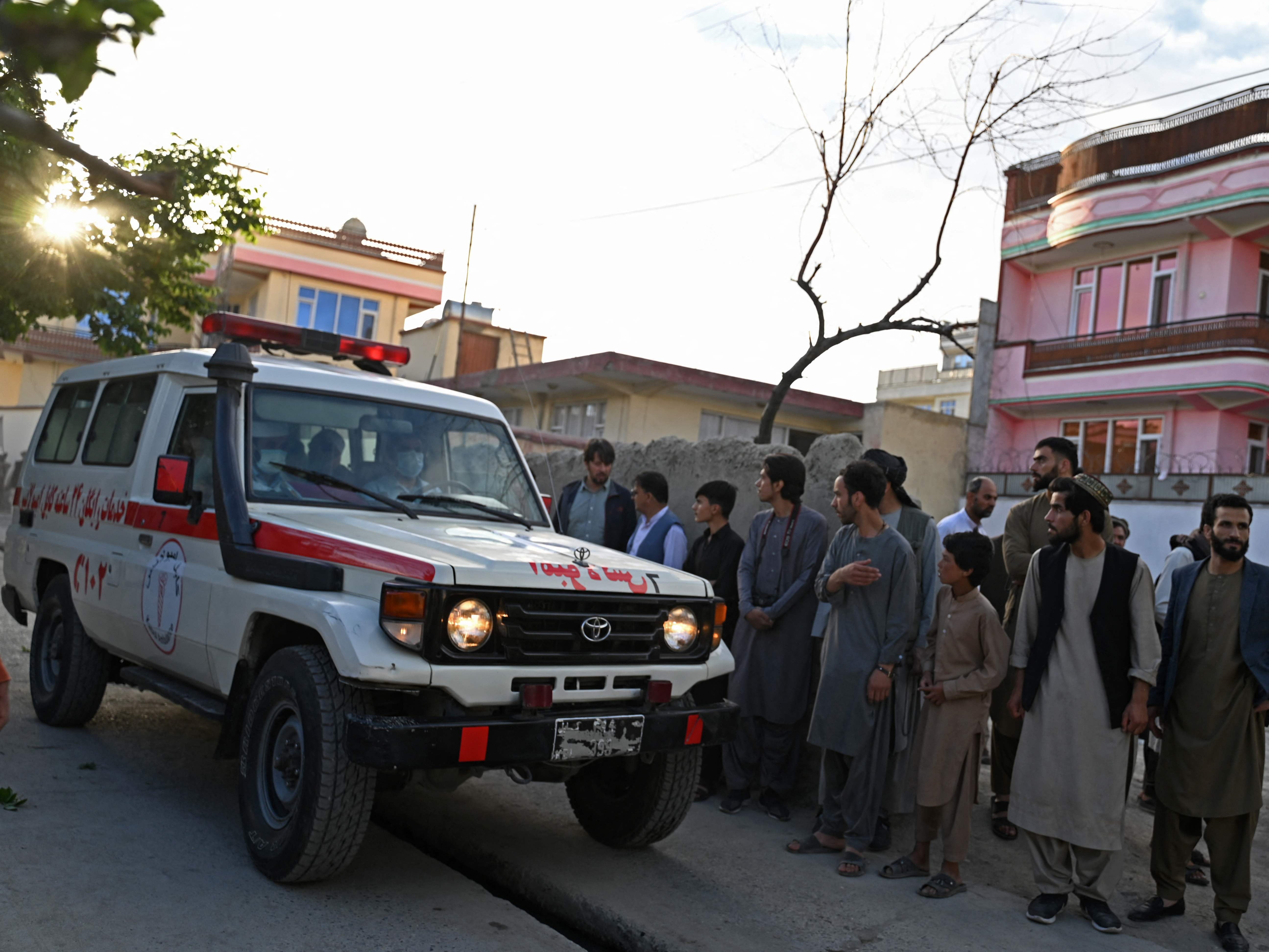 Onlookers stand next to an ambulance carrying victims near the site of a blast in Kabul