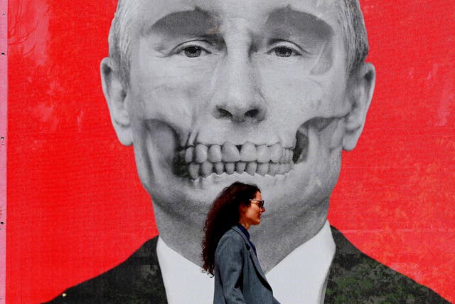 <p>A Romanian woman passes by in front a printed mesh depicting Russian president Vladimir Putin</p>