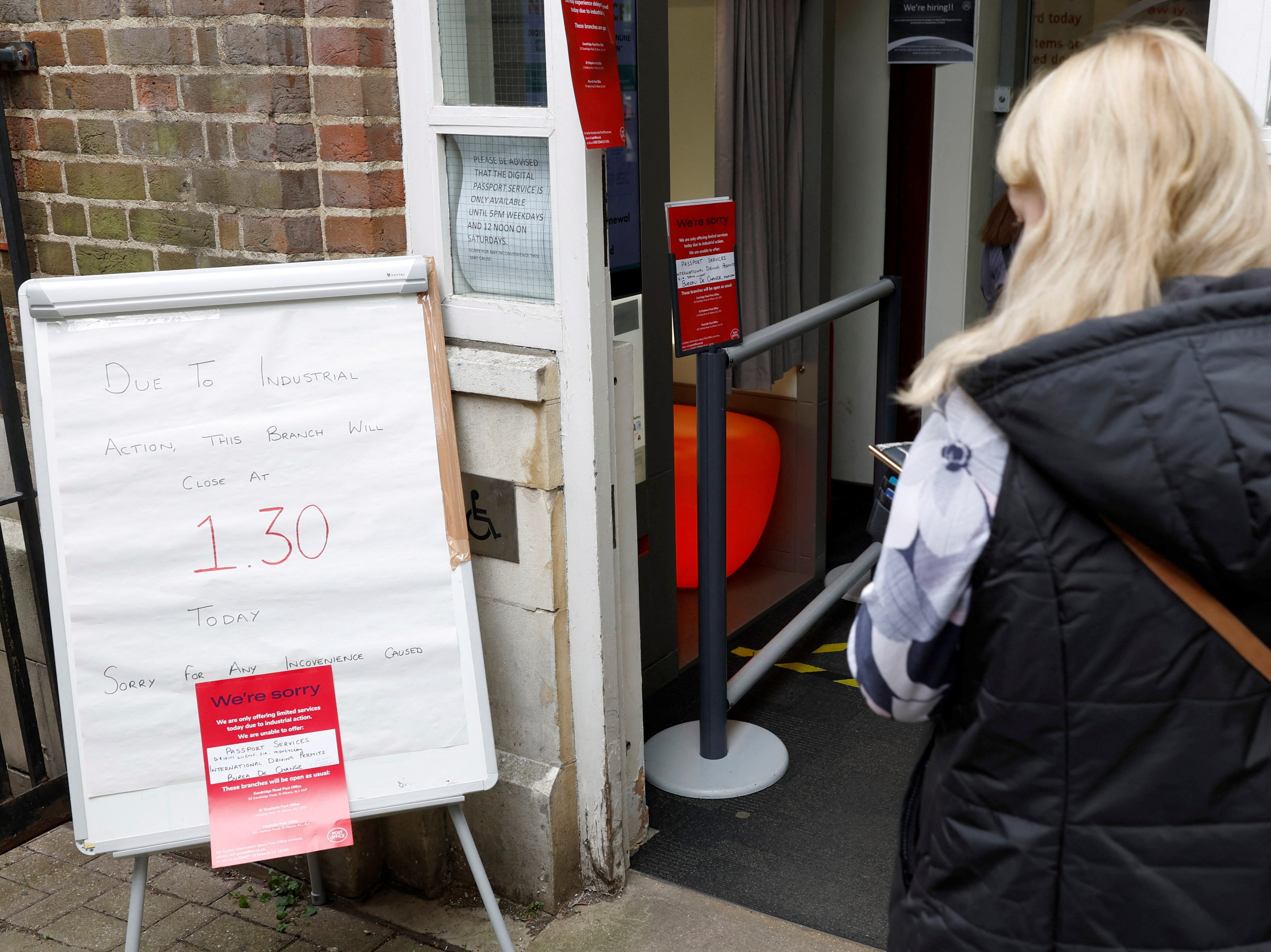 A woman walks past a sign informing customers of a Post Office branch closure due to industrial action, in St Albans, Hertfordshire