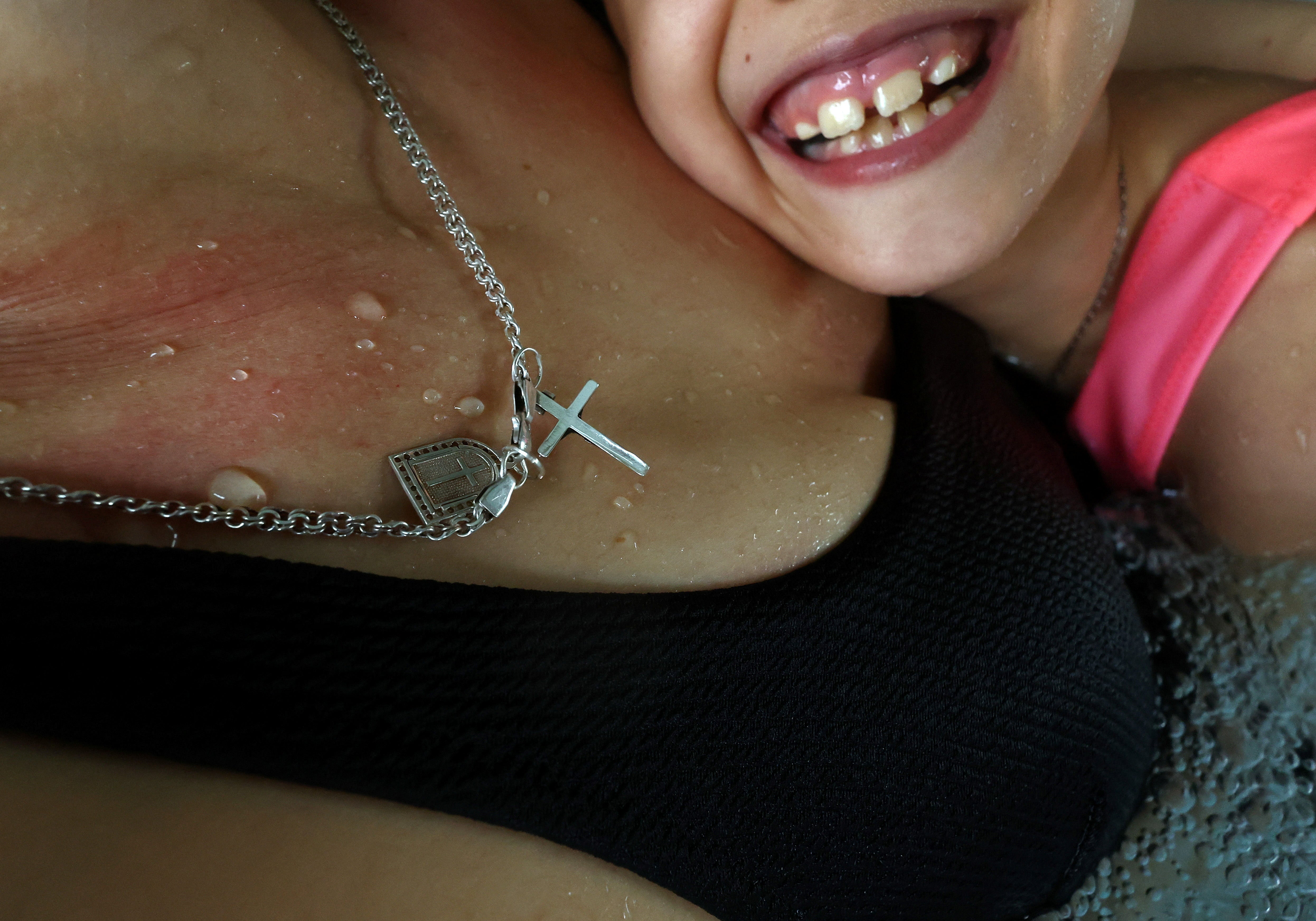 A religious necklace hangs from the neck of Alexandra, as she swims with her daughter