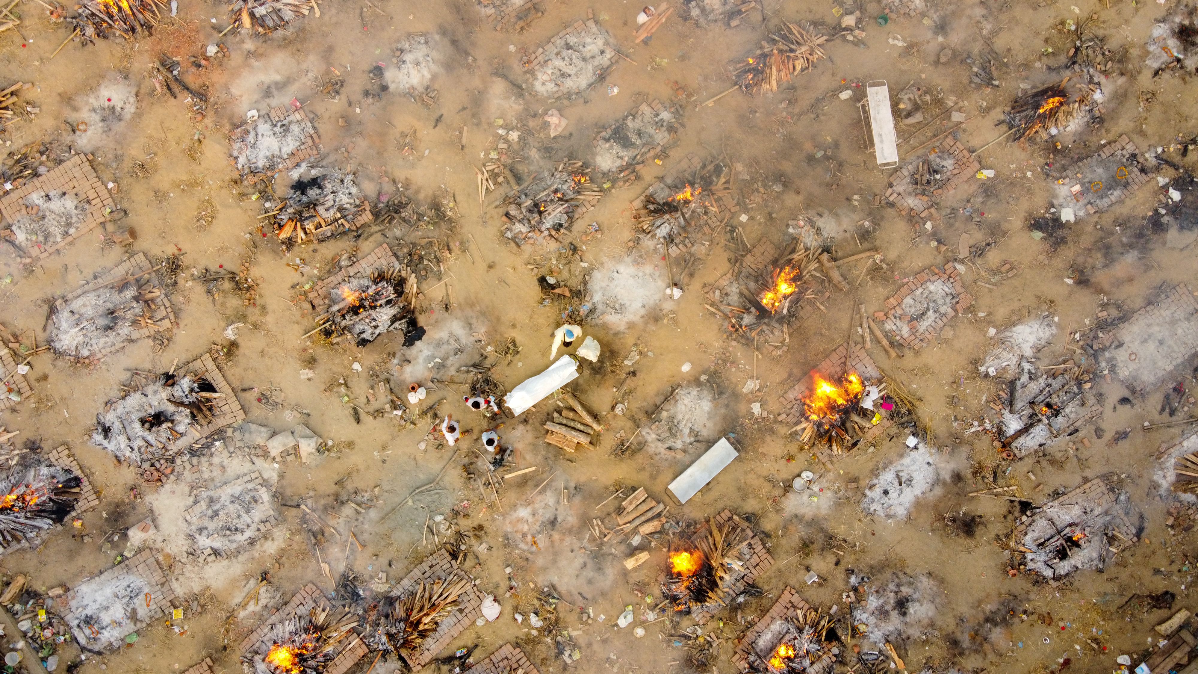 In this aerial picture taken on April 26, 2021, family members and relatives stand around the body of a victim who died of the Covid-19 coronavirus at a cremation ground in New Delhi