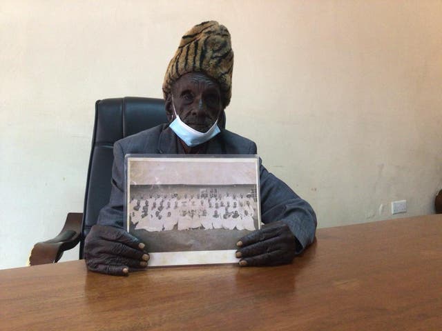 <p>The oldest survivor seeking redress, Kibore Cheruyiot Ng’asura, holds a photo taken when he was around 17 years old of him and his other clan members while they were being held at the Kericho Detention centre by British Colonial officers</p>
