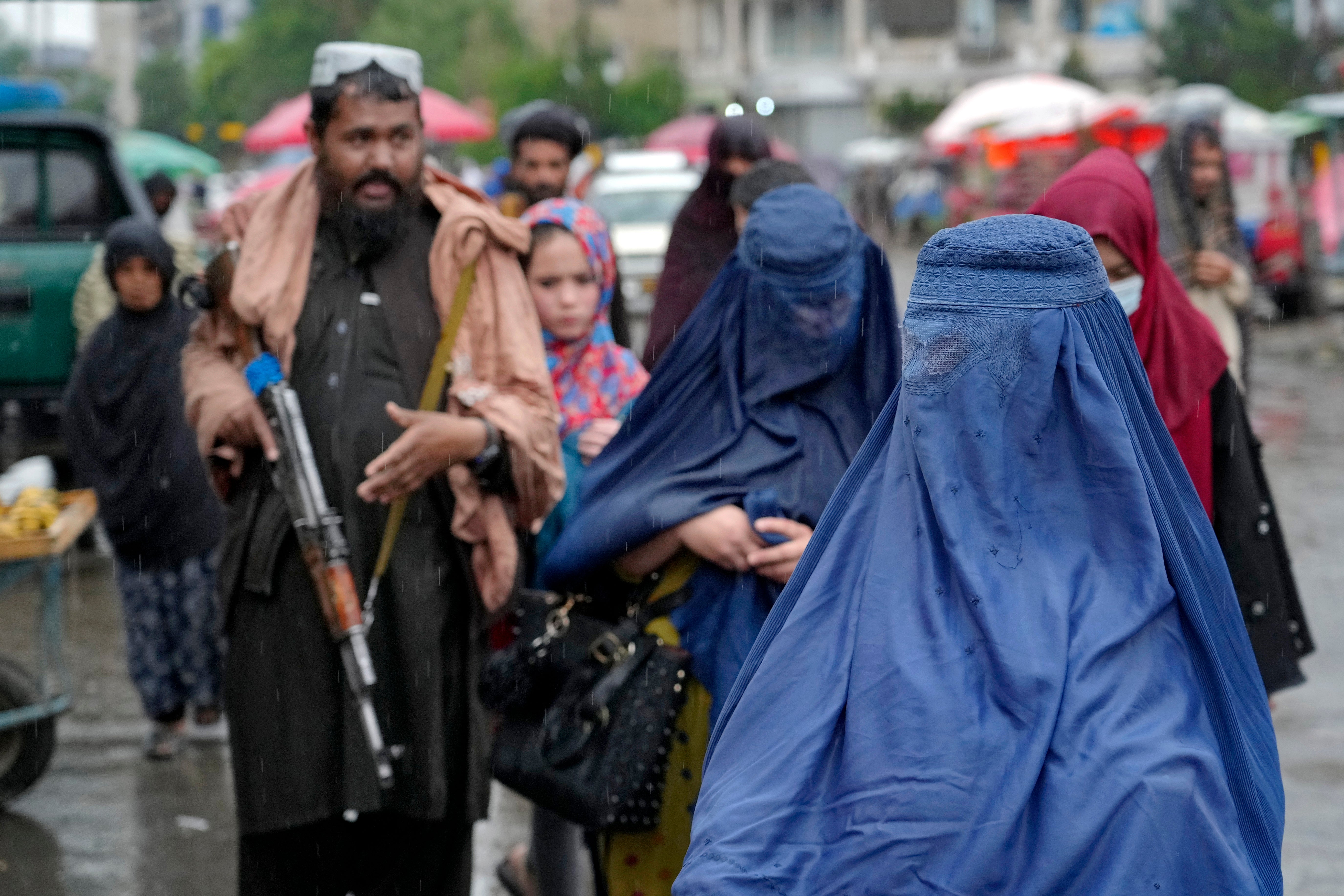 Women walk through the old market as a Taliban fighter stands guard in Kabul