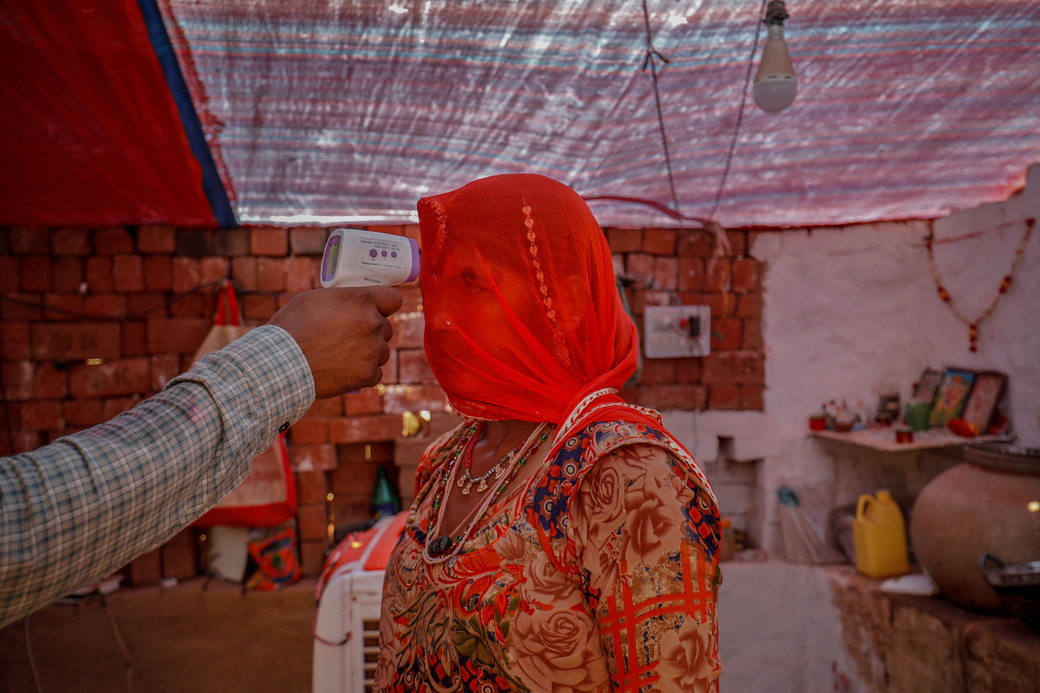 A healthcare worker checks the temperature of a woman inside her hut during a vaccination drive for workers at a brick kiln in April 2021