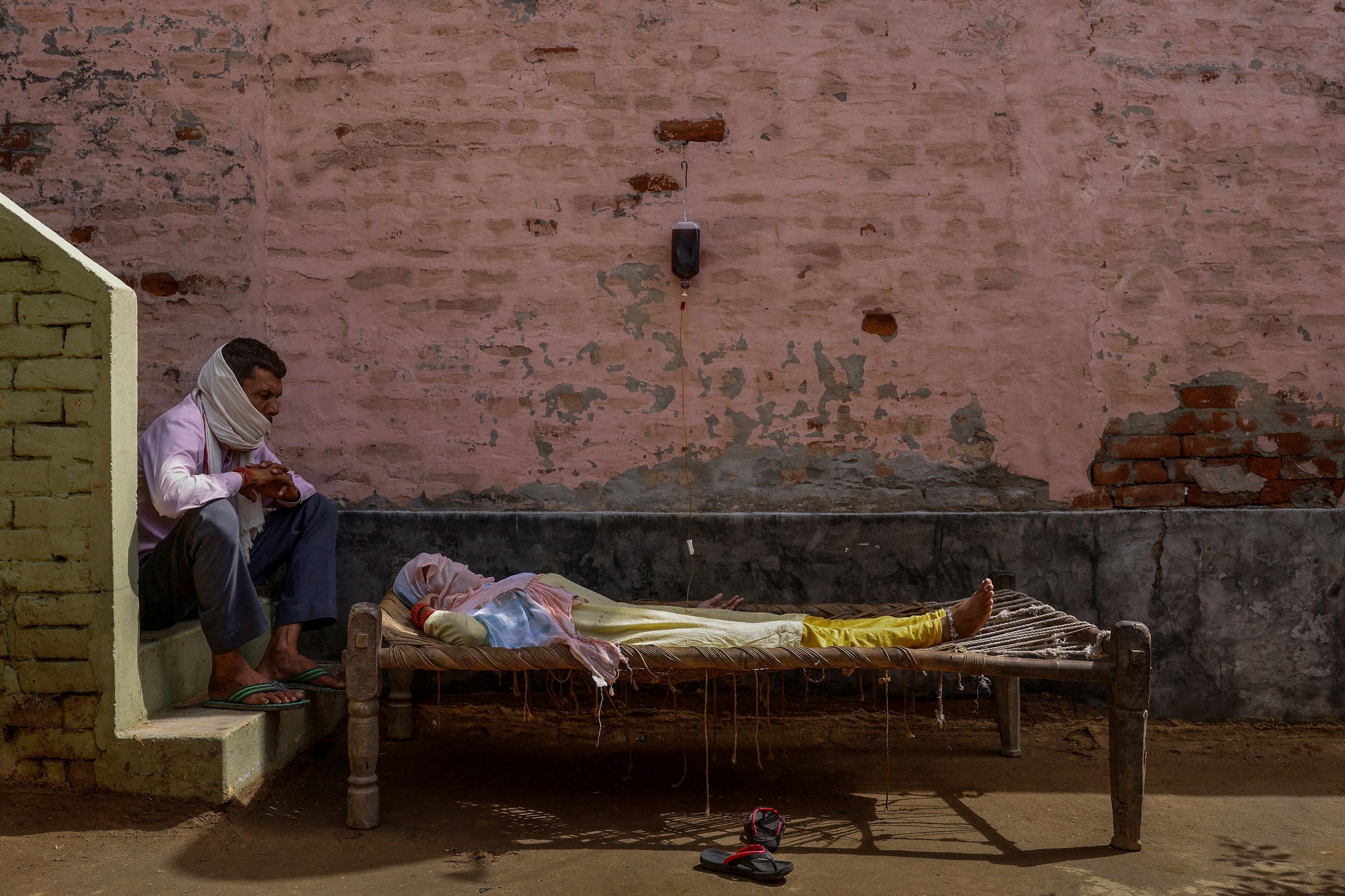A man sits next to his wife, who was suffering from a high fever, as she intravenously receives rehydration fluid at a makeshift clinic in Parsaul village, Uttar Pradesh on 22 May 2021