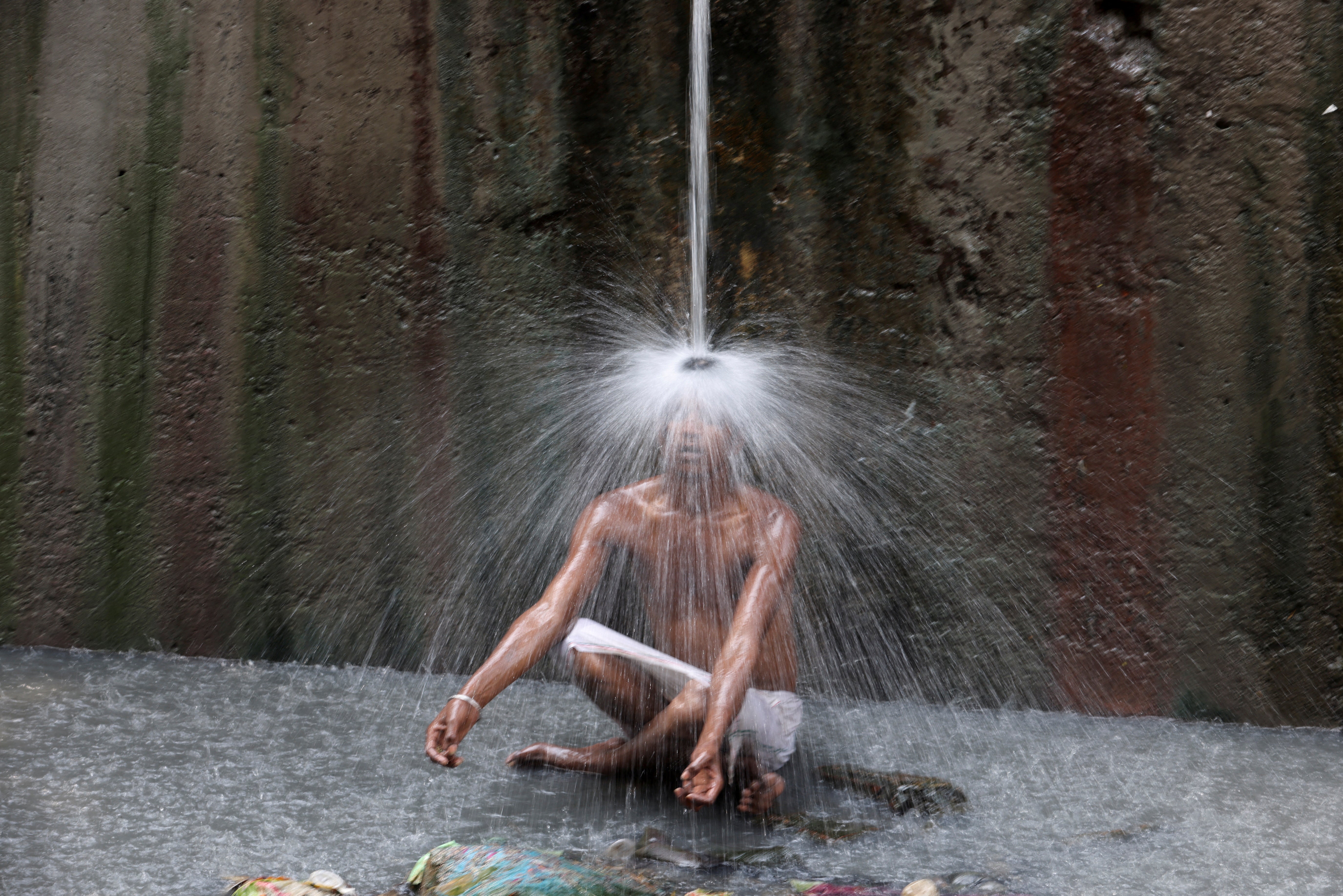 A man cools off under a pipe of flowing water on a hot day in New Delhi, India, on Wednesday
