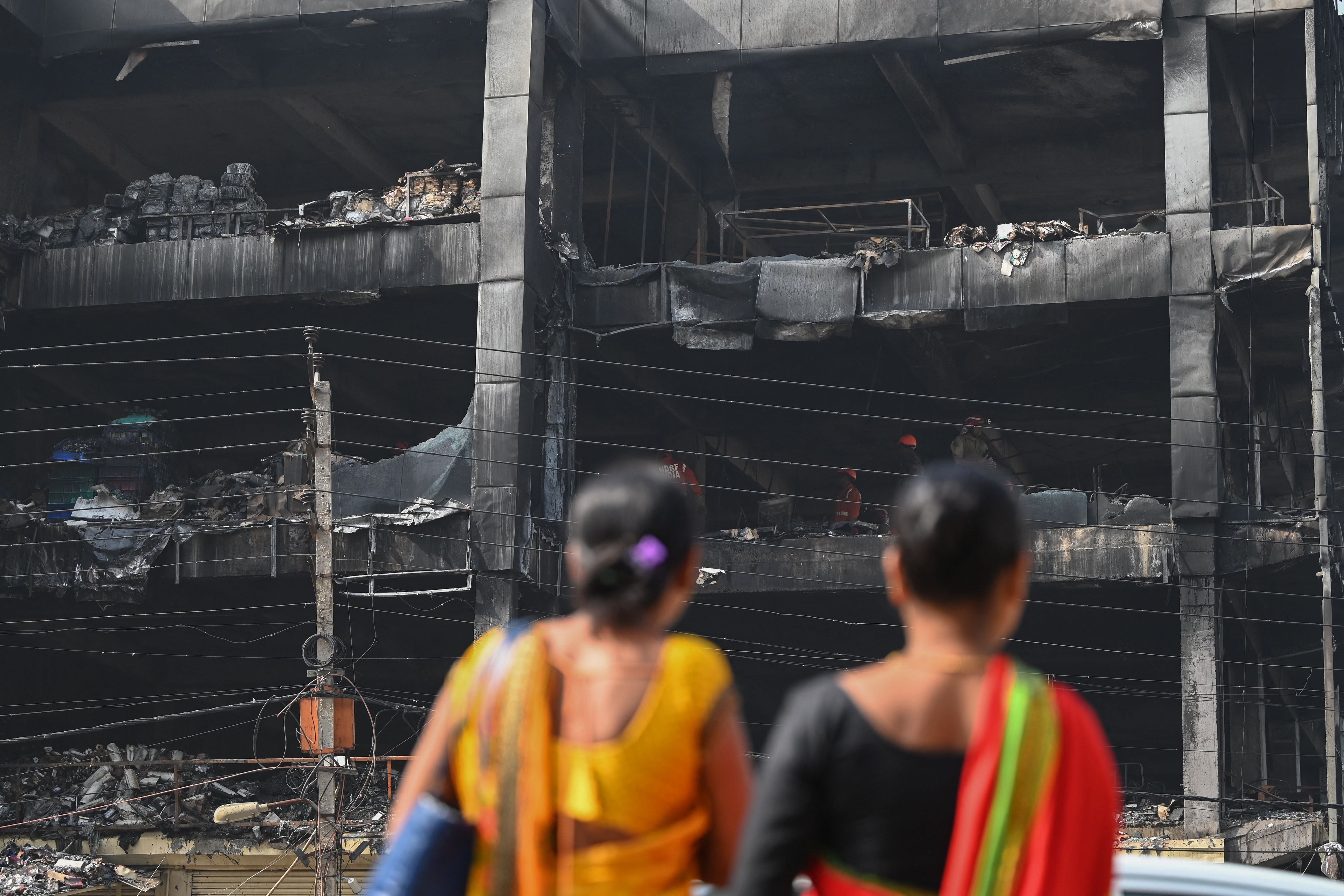 Onlookers gather outside a burn down commercial building a day after a fire broke out, in New Delhi