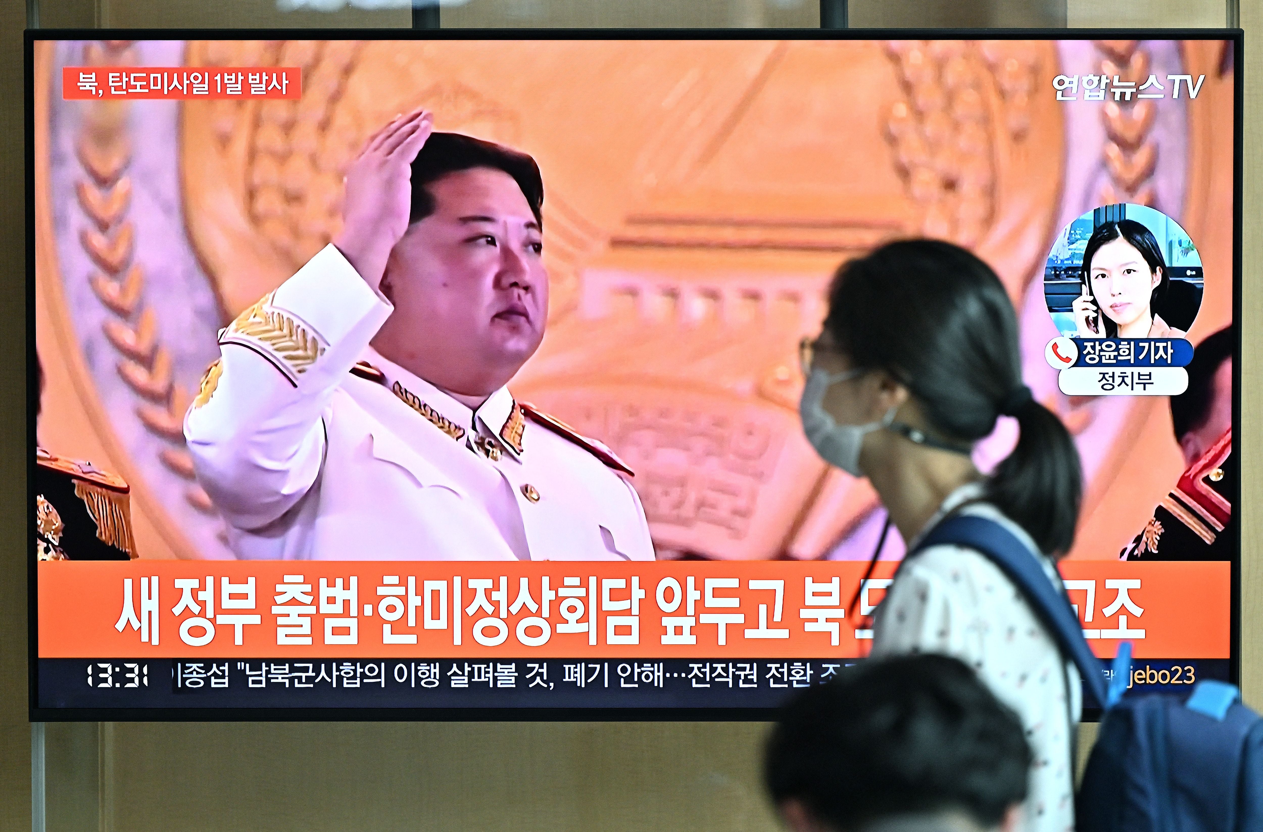 A woman walks past a television screen showing a news broadcast with file footage of North Korean leader Kim Jong Un, at a railway station in Seoul