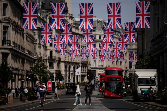 <p>People cross Regent Street, decorated with flags to mark the upcoming platinum jubilee</p>