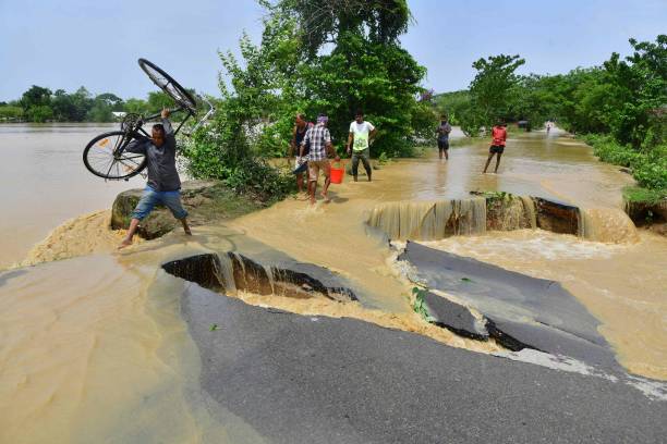 A man carrying his bicycle wades along a road partially damaged due to flooding in Nagaon district on 19 May